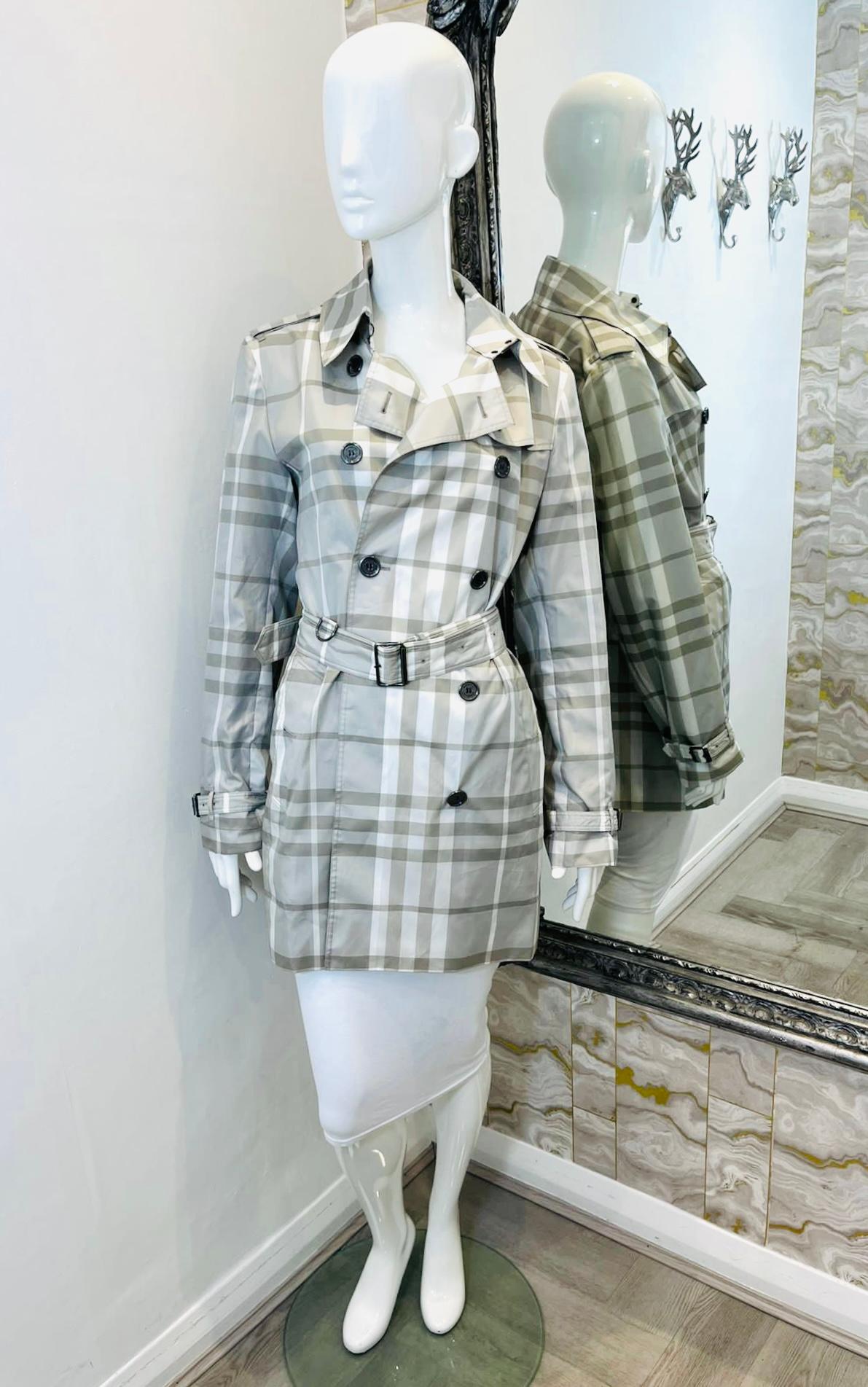 Burberry Brit Nova Check Trench Coat

Classic, lightweight trench coat designed with plaid check pattern in grey.

Detailed with double-breasted style and belted waist.

Featuring black 'Burberry' logo engraved buttons, shoulder epaulettes and