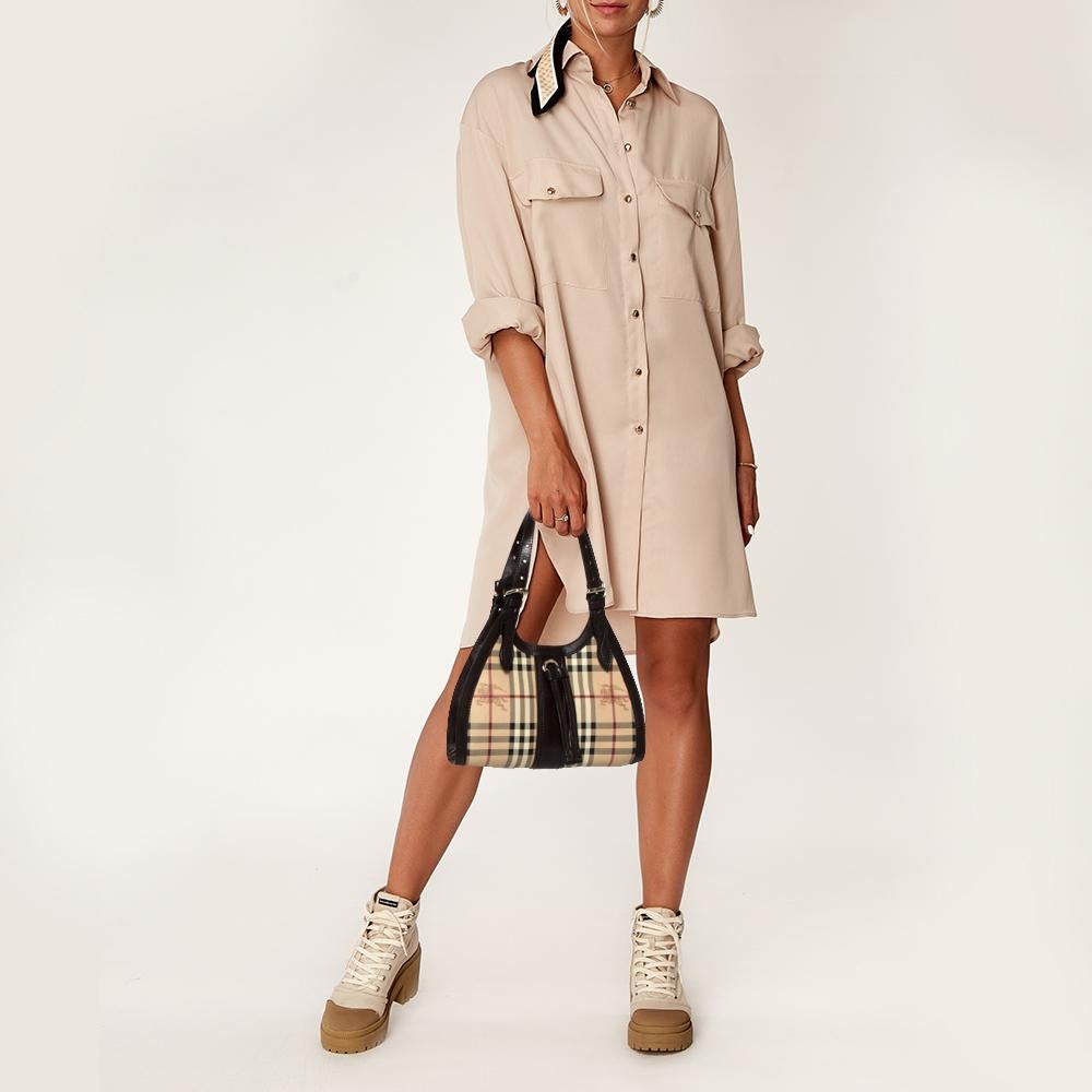 Well-made and captivating, this baguette bag is from Burberry. It has been crafted from brown & beige Haymarket check PVC & leather. The bag is equipped with a well-sized canvas interior, shoulder handles, and gold-tone hardware