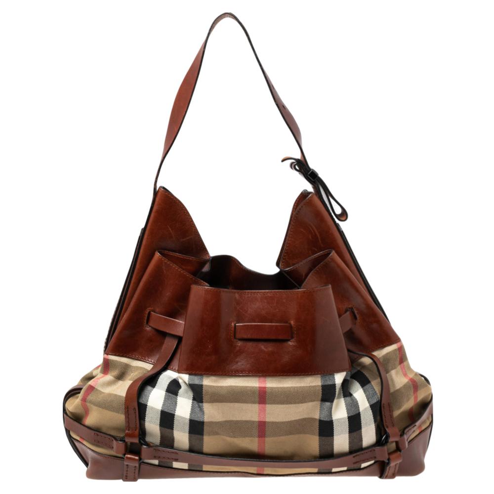 Burberry's Bridle hobo is designed in the brand's signature House Check canvas and completed with brown leather trims. The capacious size of this bag can hold all your essentials in an organized manner. It features an open-top style and comes with a