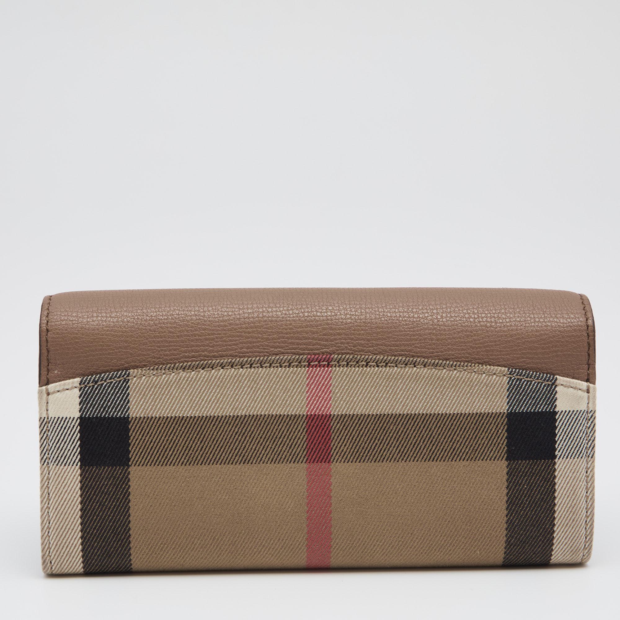 This Burberry continental wallet is crafted from fabric and leather. The front flap has a buttoned closure that opens to a well-sized interior having two open compartments and slip pockets for you to arrange your cards and bills securely. Perfect