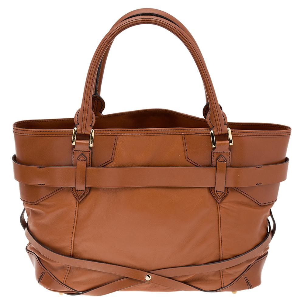 This stylish Bridle Lynher tote from the House of Burberry has been crafted from brown leather into a stylish silhouette. It is finished with gold-toned hardware, buckled detailing, and dual handles. A spacious nylon-lined interior is one of the