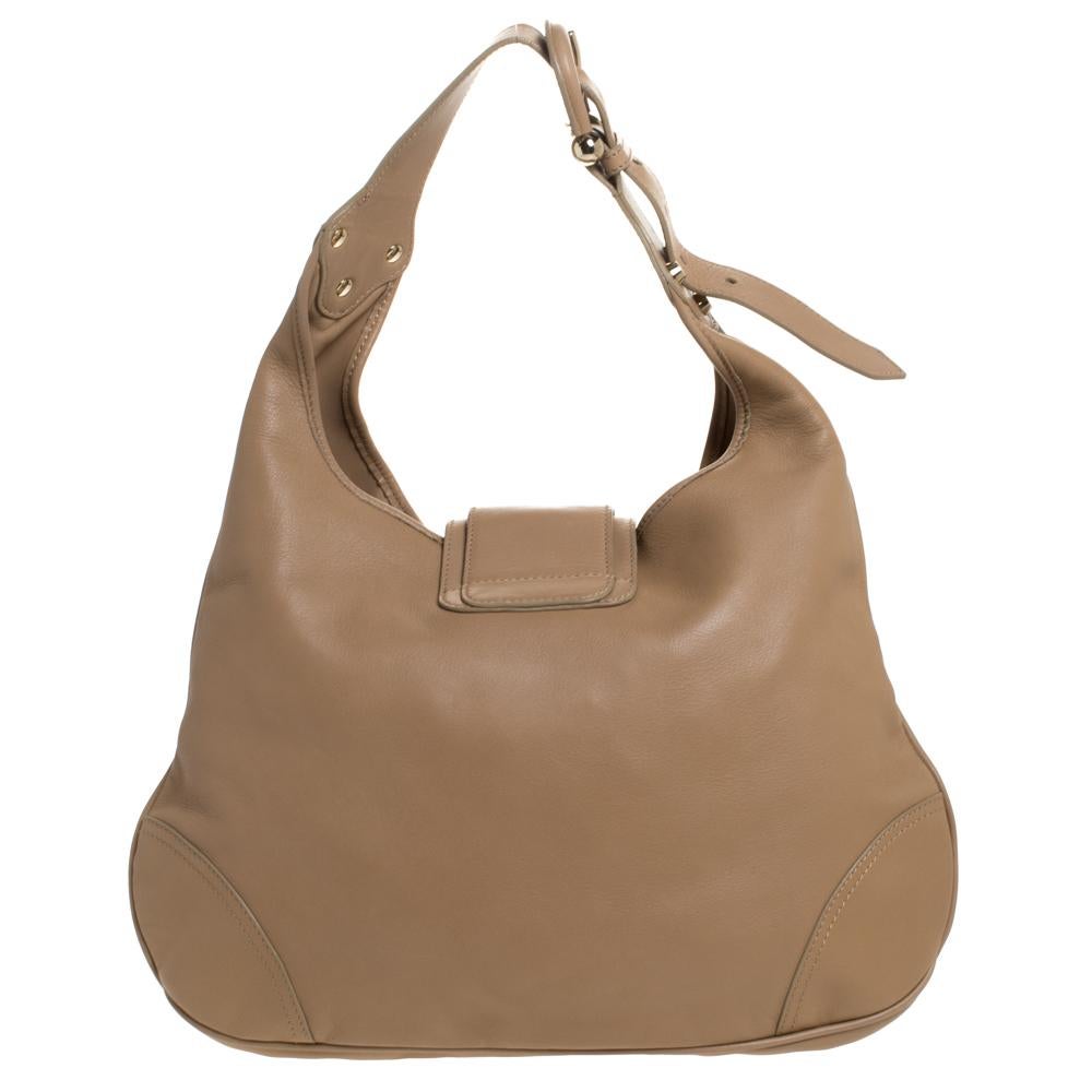 This fashionable hobo bag by Burberry is all you need to perfectly complement your attire. Crafted from quality leather, it comes in a lovely shade of brown. Itis styled with one handle, a large buckled strap as the closure that opens to reveal a