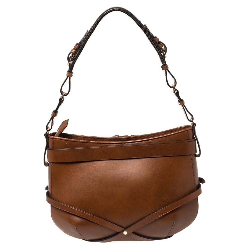 This stylish hobo from Burberry has been crafted from brown leather. The zip-top closure opens to a canvas-lined interior that is spacious enough to hold your everyday essentials. The bag comes with a shoulder strap and belt detailing.

