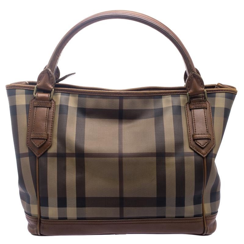 This tote from Burberry is crafted from PVC in classic smoke check and completed with leather trims. The top zip closure opens to a canvas lined interior that will hold your daily essentials and the tote is complete with dual handles. Simple in