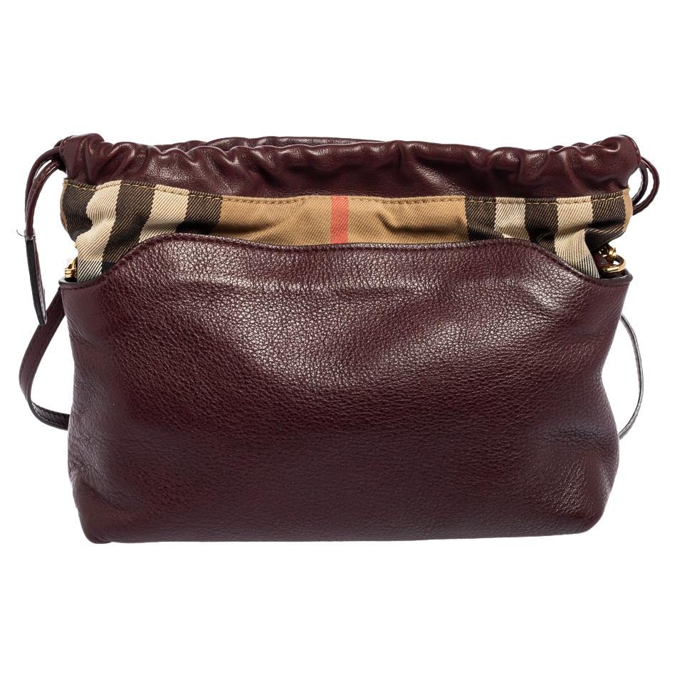 The Little Crush shoulder bag from Burberry is a fusion of utility and style. Crafted in burgundy leather, it flaunts the signature House Check canvas trim and is held by a shoulder strap. The drawstring closure secures a durable canvas-lined