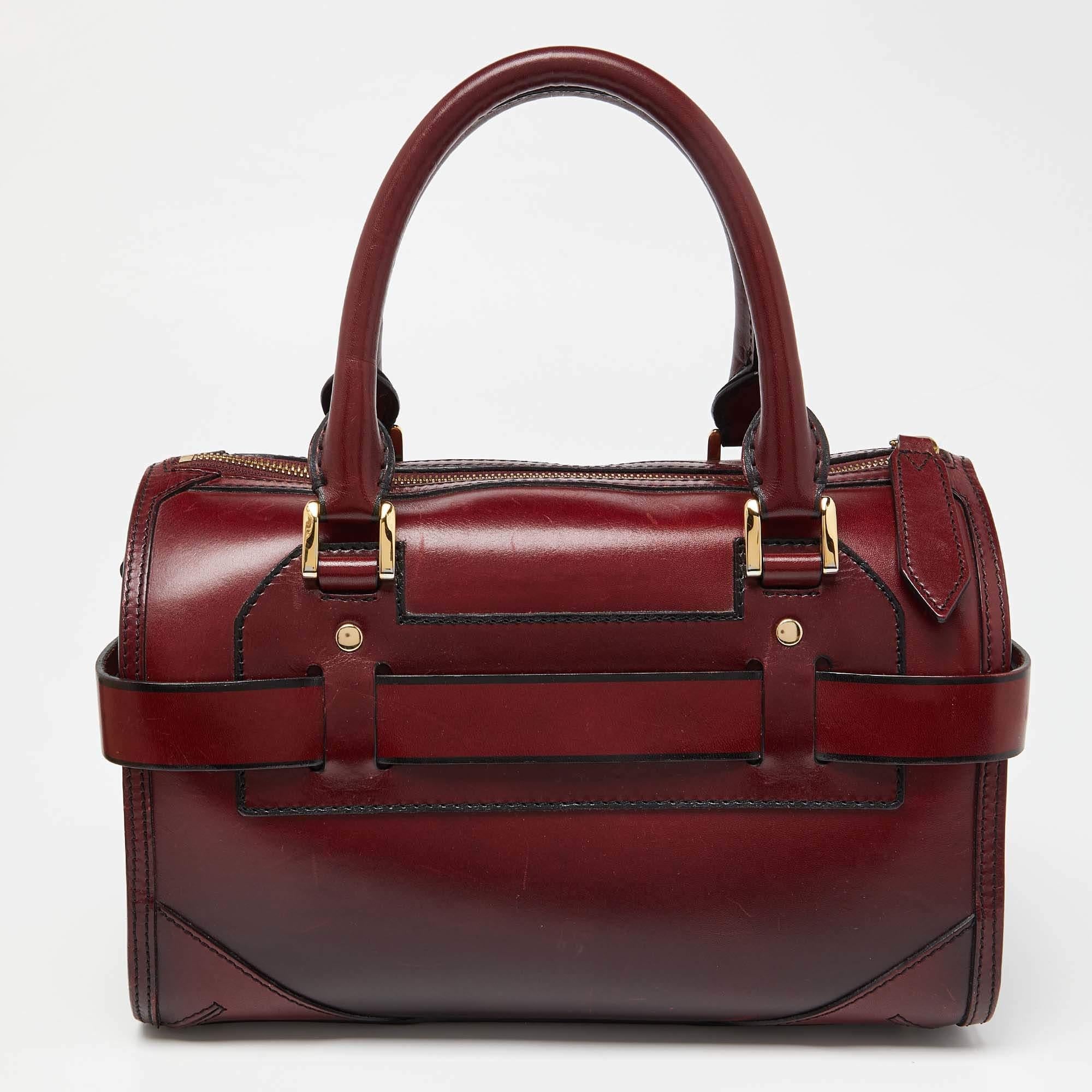 This Burberry bowler bag is a perfect everyday bag that can accommodate all your daily essentials. Crafted from burgundy leather, it is accented with gold-tone hardware. It features a logo plaque, two top handles, a shoulder strap, and a triple