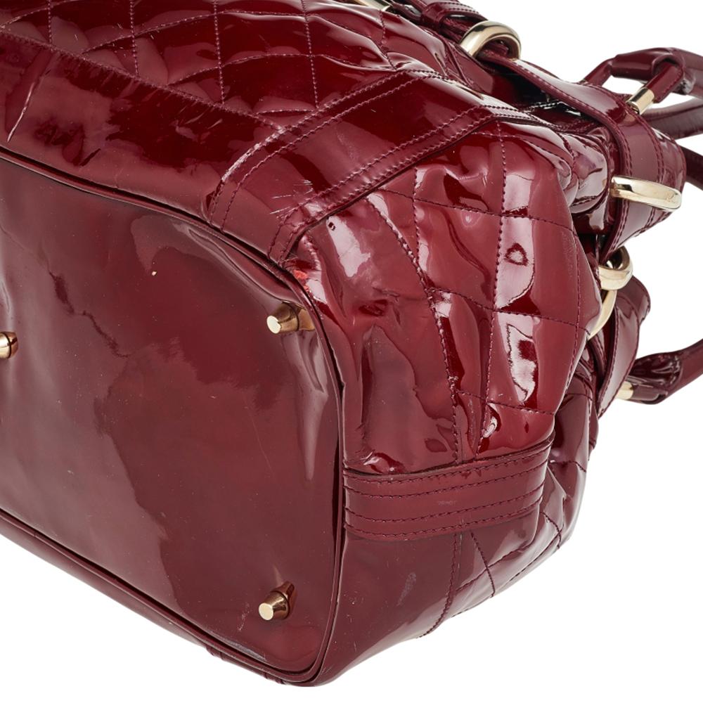 Crafted from quilted patent leather, this Burberry Prorsum Beaton bag is detailed with a fashionable belt buckle, Burberry's equestrian knight logo, and double leather handles. The easy-to-organize interior is lined with red fabric and features a