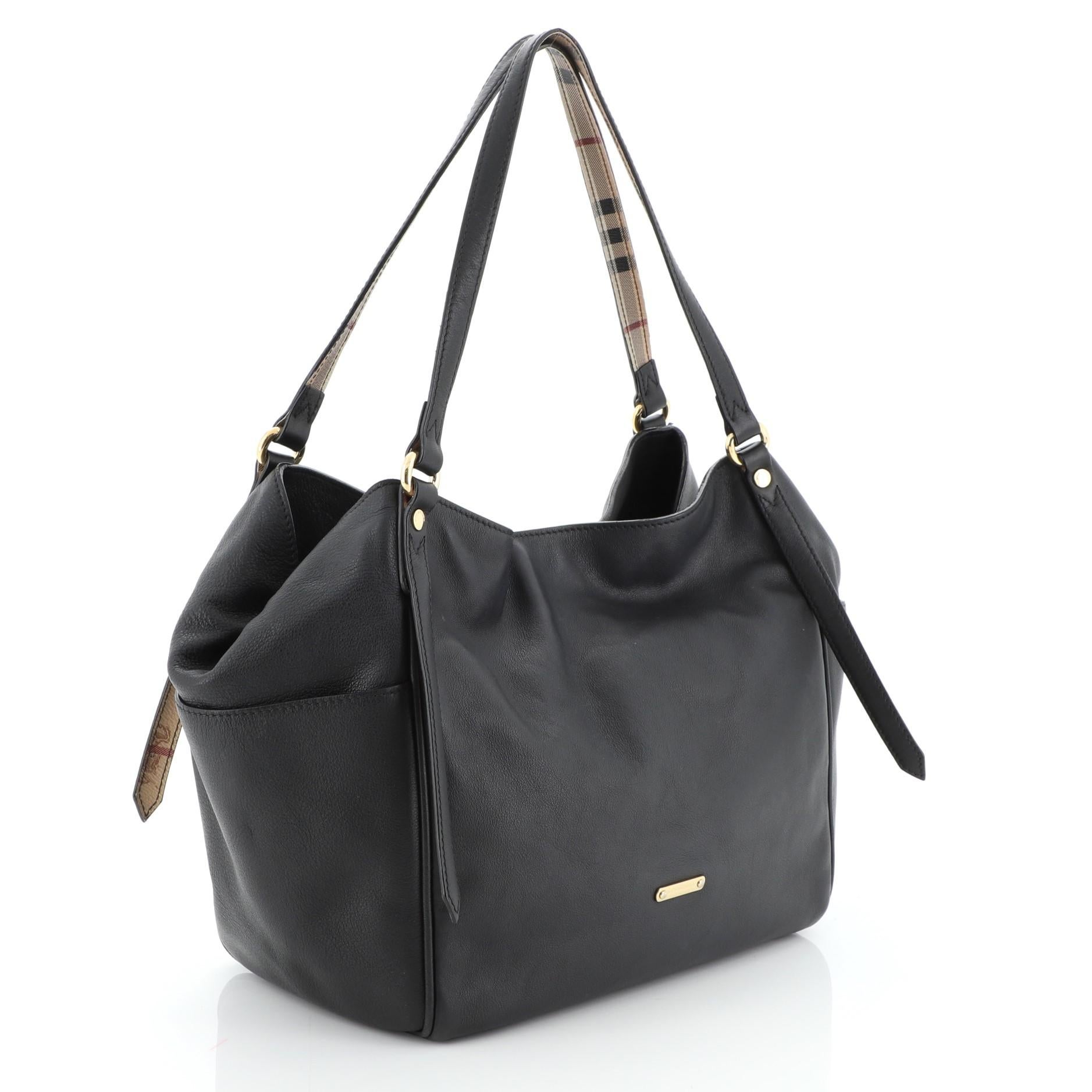 This Burberry Canterbury Tote Leather Small, crafted from black leather, features dual tall adjustable handles, Burberry logo, and gold-tone hardware. Its magnetic snap closure opens to a black fabric interior with side wall zip and slip