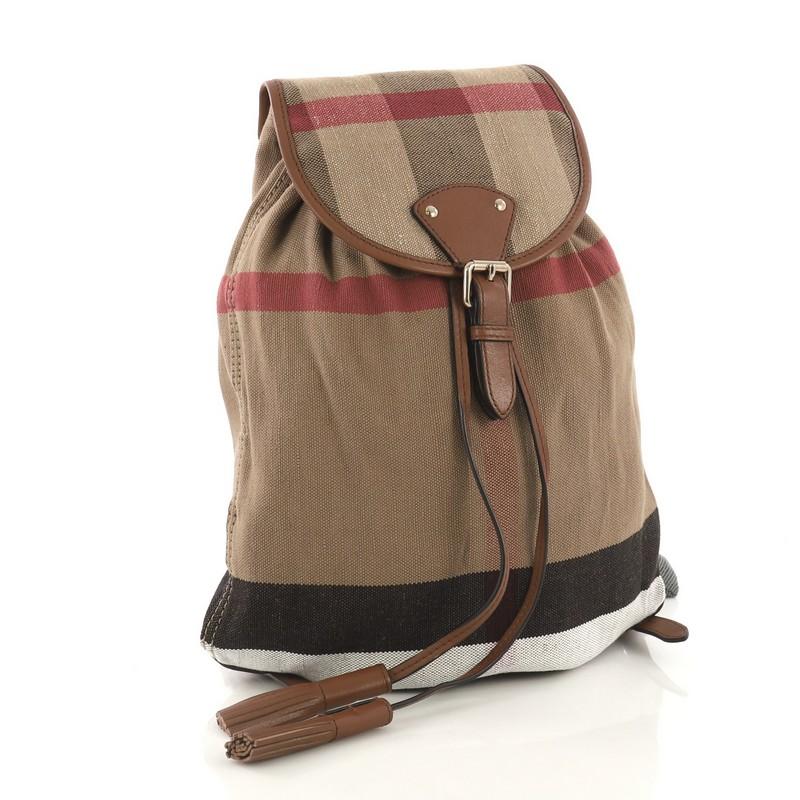 This Burberry Chiltern Backpack House Check Canvas Medium, crafted from brown house check canvas, features adjustable shoulder straps, leather trim, and gold-tone hardware. Its buckle and drawstring closure opens to a brown house check canvas