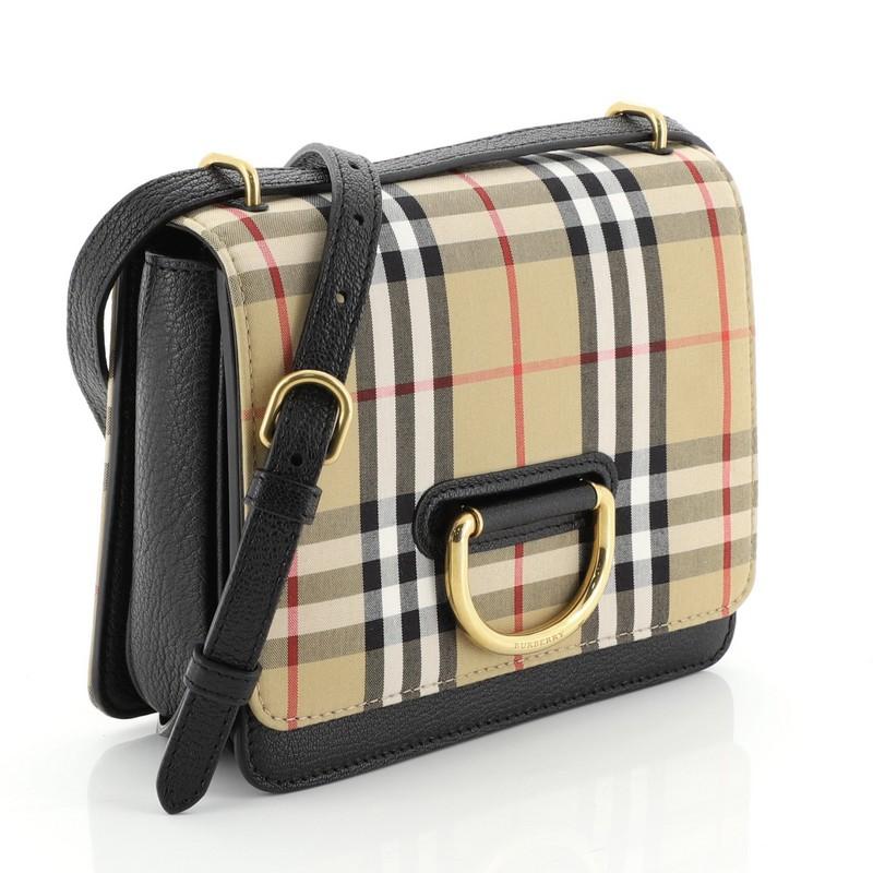 This Burberry D-Ring Shoulder Bag Vintage Check Canvas Small, crafted from check canvas and black leather, features adjustable leather strap and gold-tone hardware. Its flap opens to a brown leather interior. 

Estimated Retail Price: