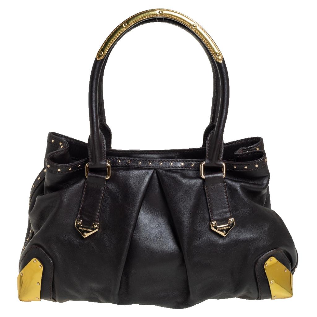 This stylish and practical tote from Burberry is crafted from dark brown leather. It comes with dual handles, studs, gold-tone hardware details, and a spacious nylon-lined interior that can hold all your daily necessities. Simple in design, the tote
