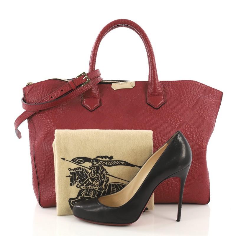 This Burberry Dewsbury Convertible Tote Check Embossed Leather Medium, crafted from red check embossed leather, features dual rolled leather handles, exterior slip pocket with magnetic closure, and gold-tone hardware. Its zip closure opens to a