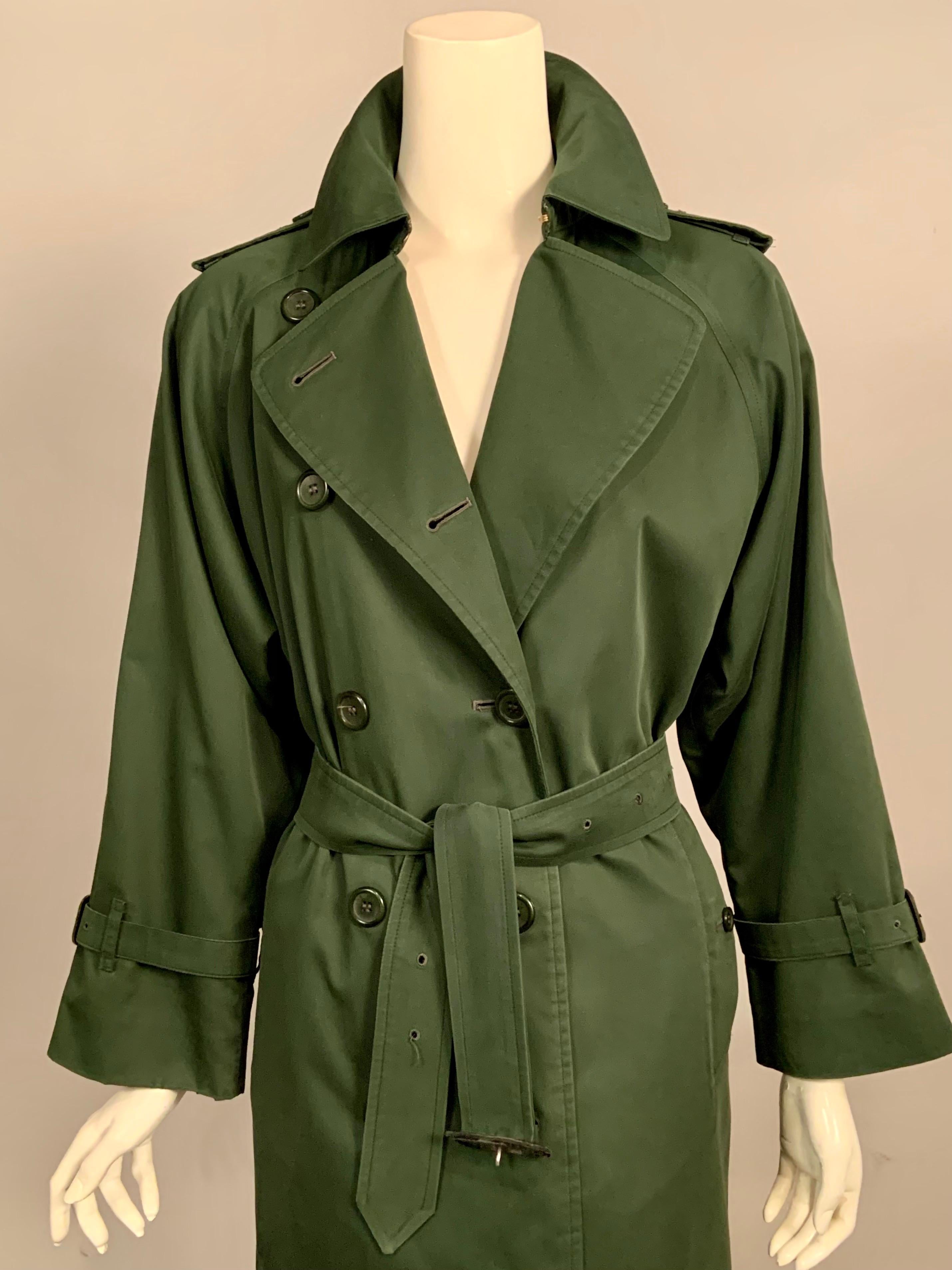 This classic Burberry dark green trench coat has shoulder epaulets, leather buckles on the sleeves, a belt with another  leather buckle, two pockets with button flaps, a green version of the iconic Burberry plaid lining and a removeable  zip in