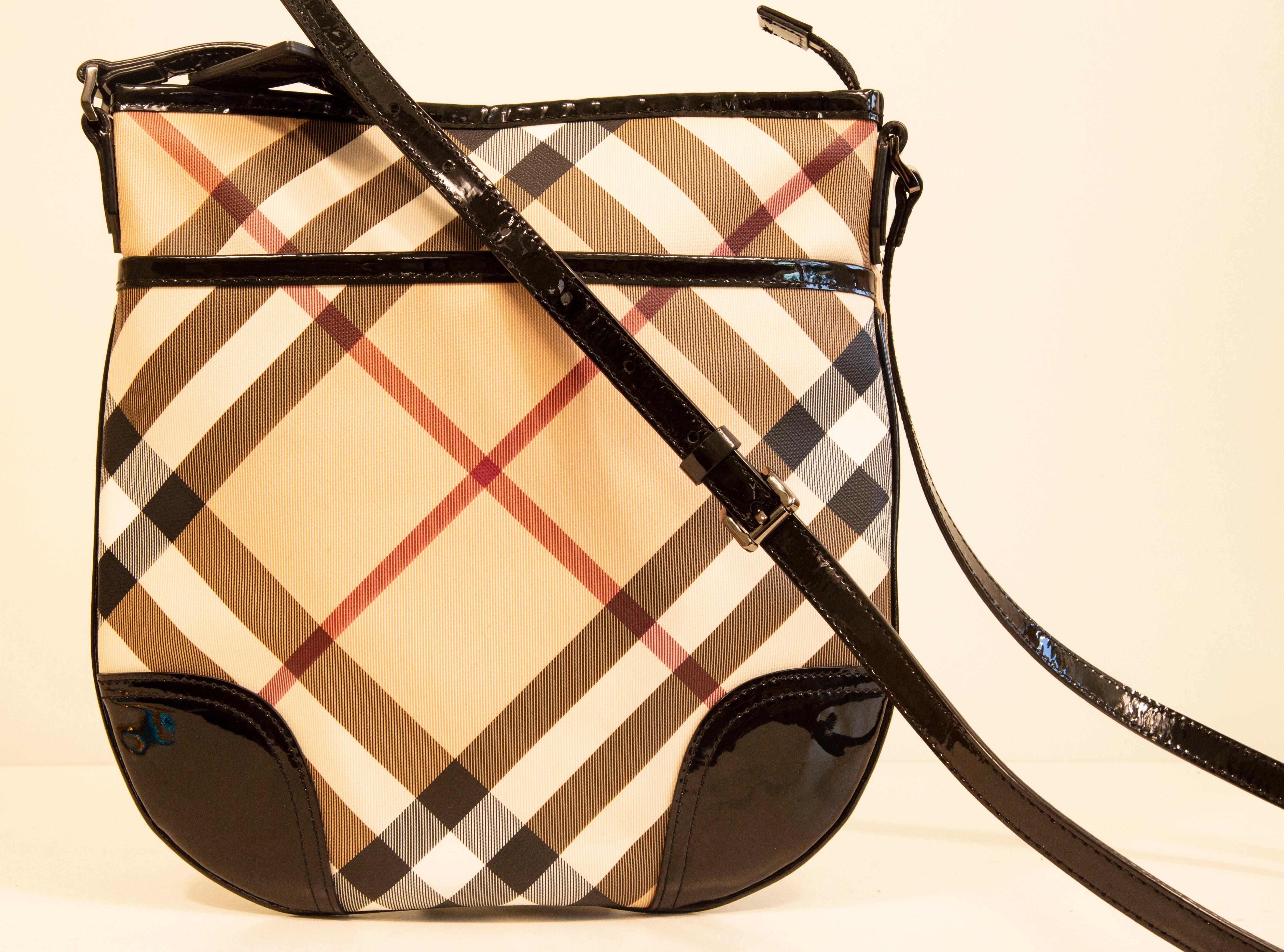 Burberry Dryden crossbody bag made of coated canvas with black patent leather trim and shiny pewter toned hardware. The exterior features the Burberry Nova Check pattern. The interior is lined with beige fabric, and next to the major compartment it