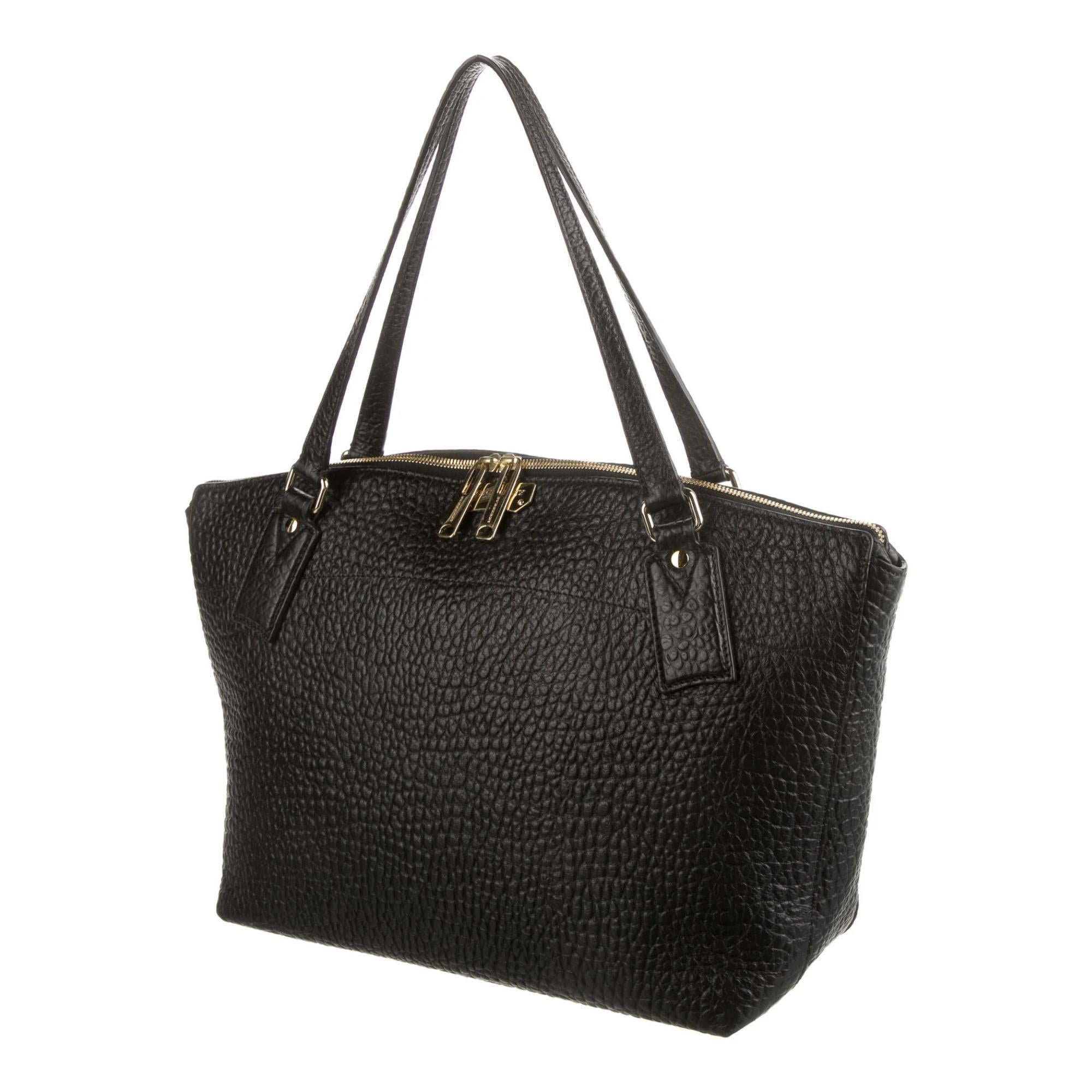 Introducing this Burberry tote in strong textured black leather. The bag features pebbled leather construction, gold-tone hardware, dual flat leather handles, top zip closure and protective feet at the base. The bag is finished with logo jacquard
