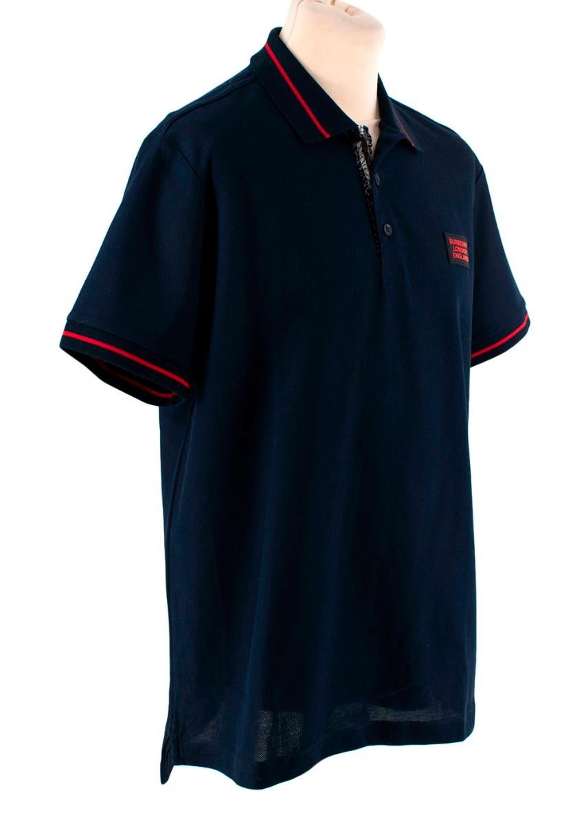 Burberry Grenford Navy Cotton Pique Red Trim Polo
 

 - Navy cotton pique polo shirt
 - Red-tone trim accent to the ribbed collar and cuffs
 - Signature striped and monogram embellished placket
 - Black and red rubber applique to the chest with