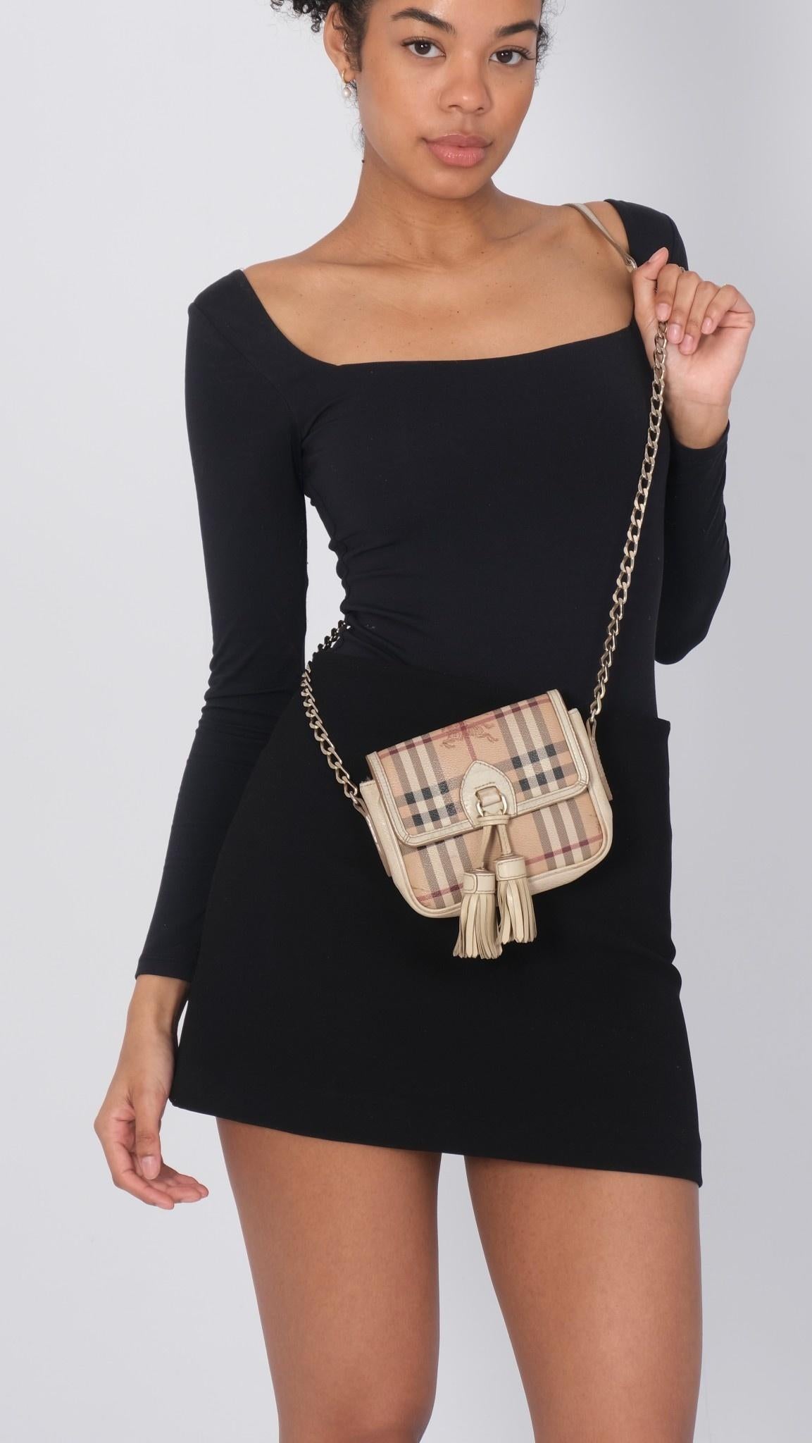 Ce mini sac est réalisé en toile enduite avec l'imprimé à carreaux de la maison Burberry. Le sac présente des détails et des garnitures en cuir, deux glands décoratifs suspendus sur le devant, une fermeture à bouton-pression sur le rabat, une