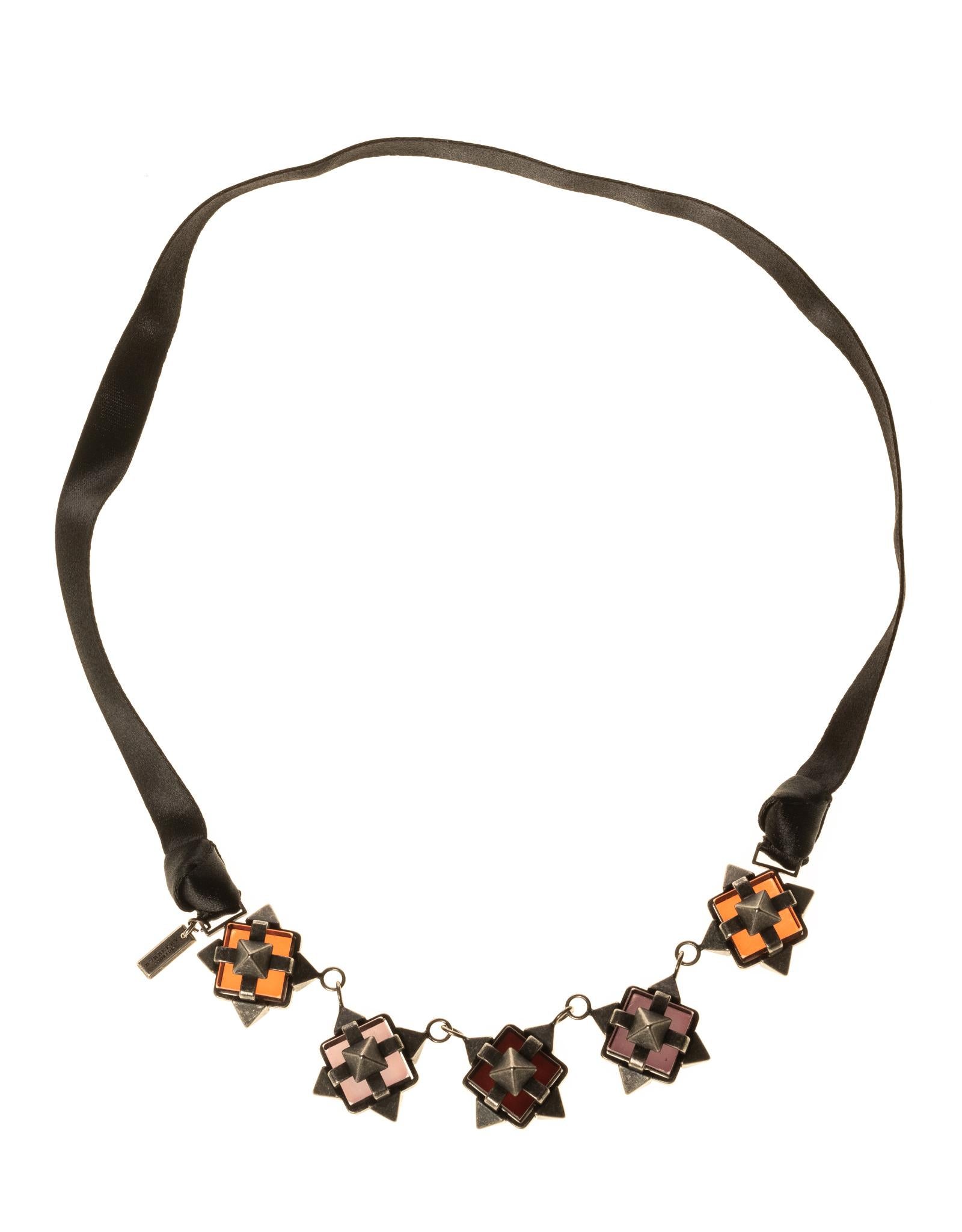 This Burberry necklace is made of a beautiful black grosgrain ribbon with five metal and poured glass ornaments connected with a chain. The ornaments look black and grey with normal light, but the poured glass has subtle color that changes depending