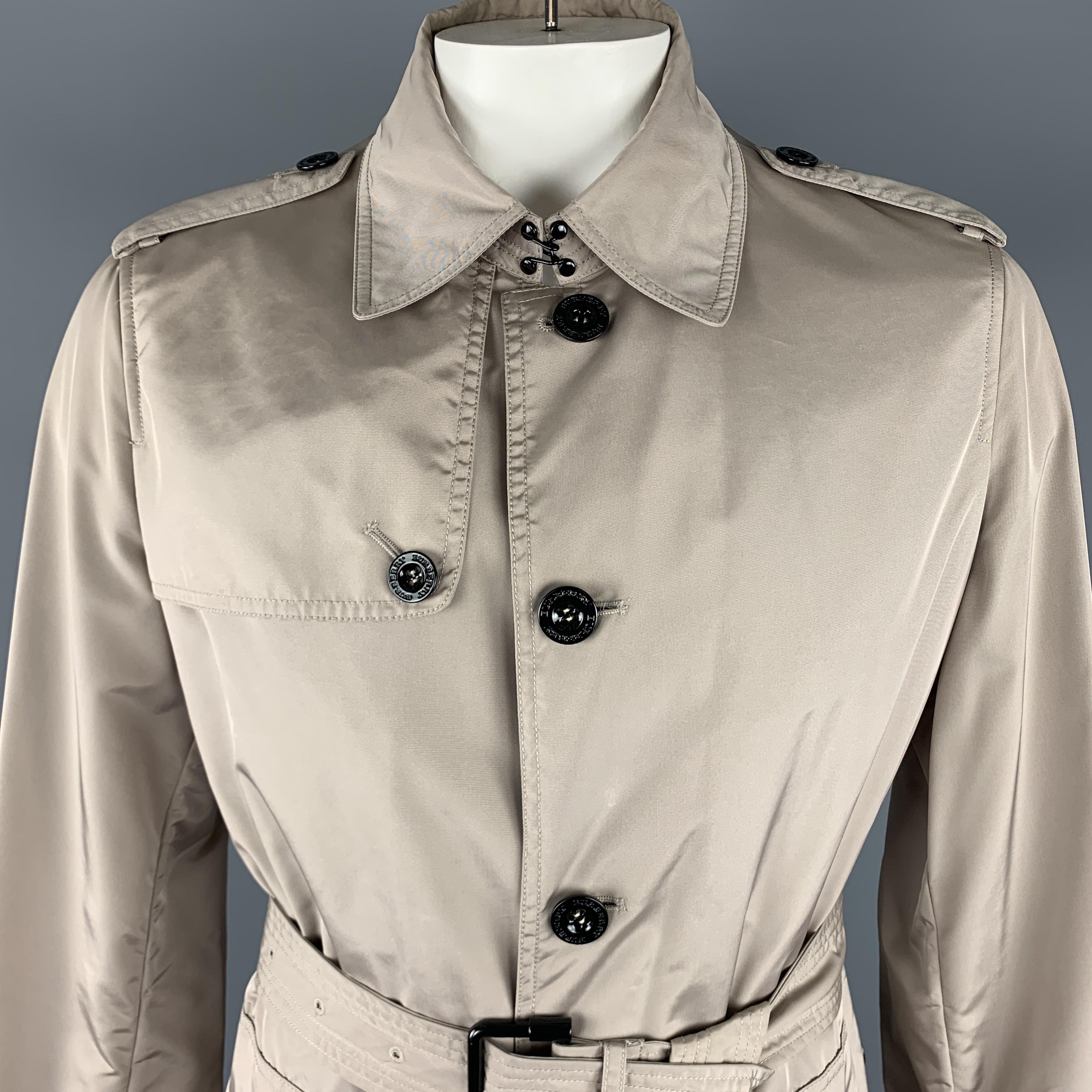 BURBERRY LONDON trenchcoat comes in a taupe tone in a solid nylon material, with a pointed collar, epaulettes, buttoned front, single breasted, belted cuffs and waist, patch pockets and a single vent at back, unlined. Includes the original garment