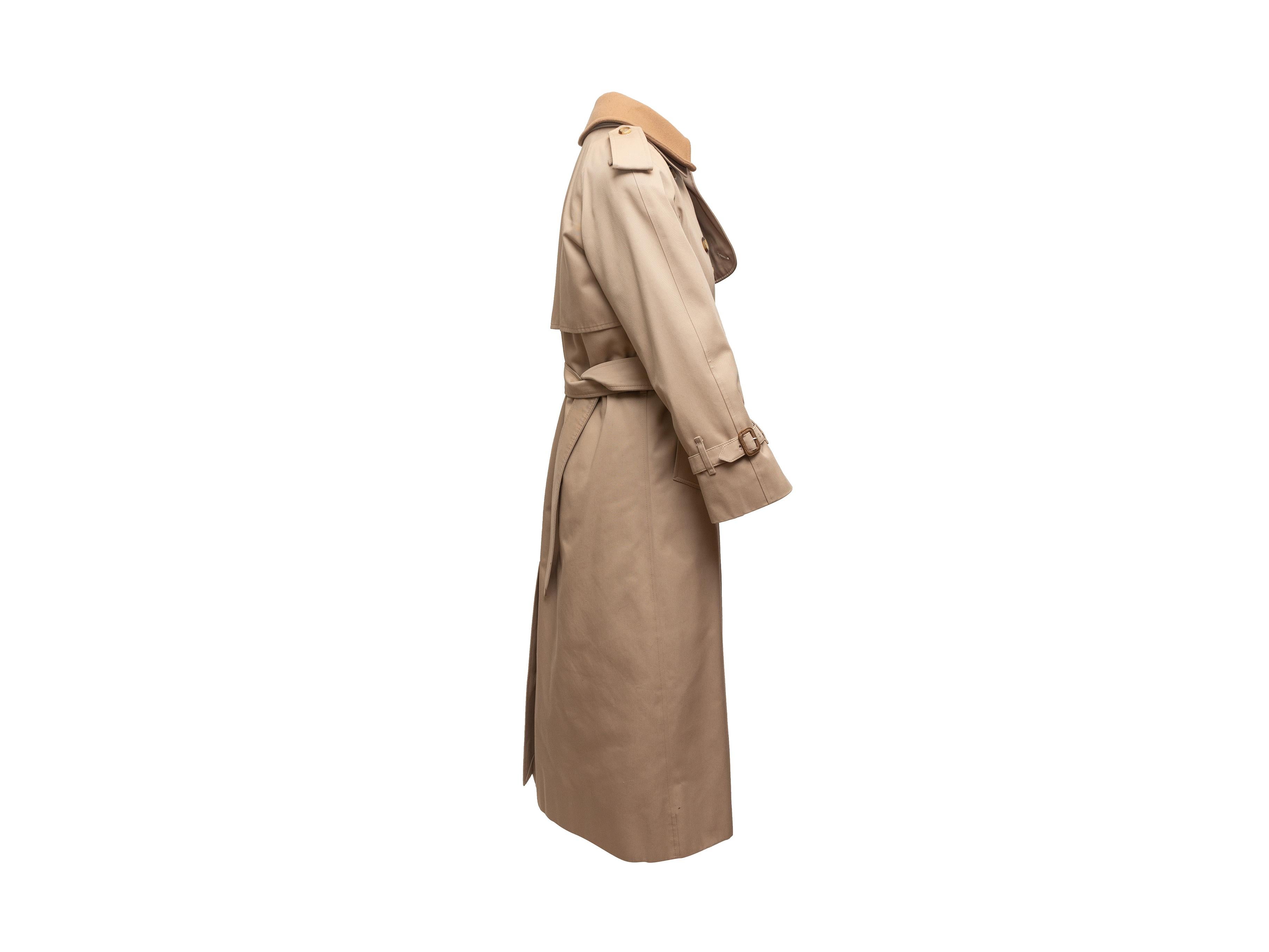 Product details: Tan long double-breasted trench coat by Burberry London. Pointed collar. Dual hip pockets. Belt at waist. Tan wool lining. Button closures at front. 36