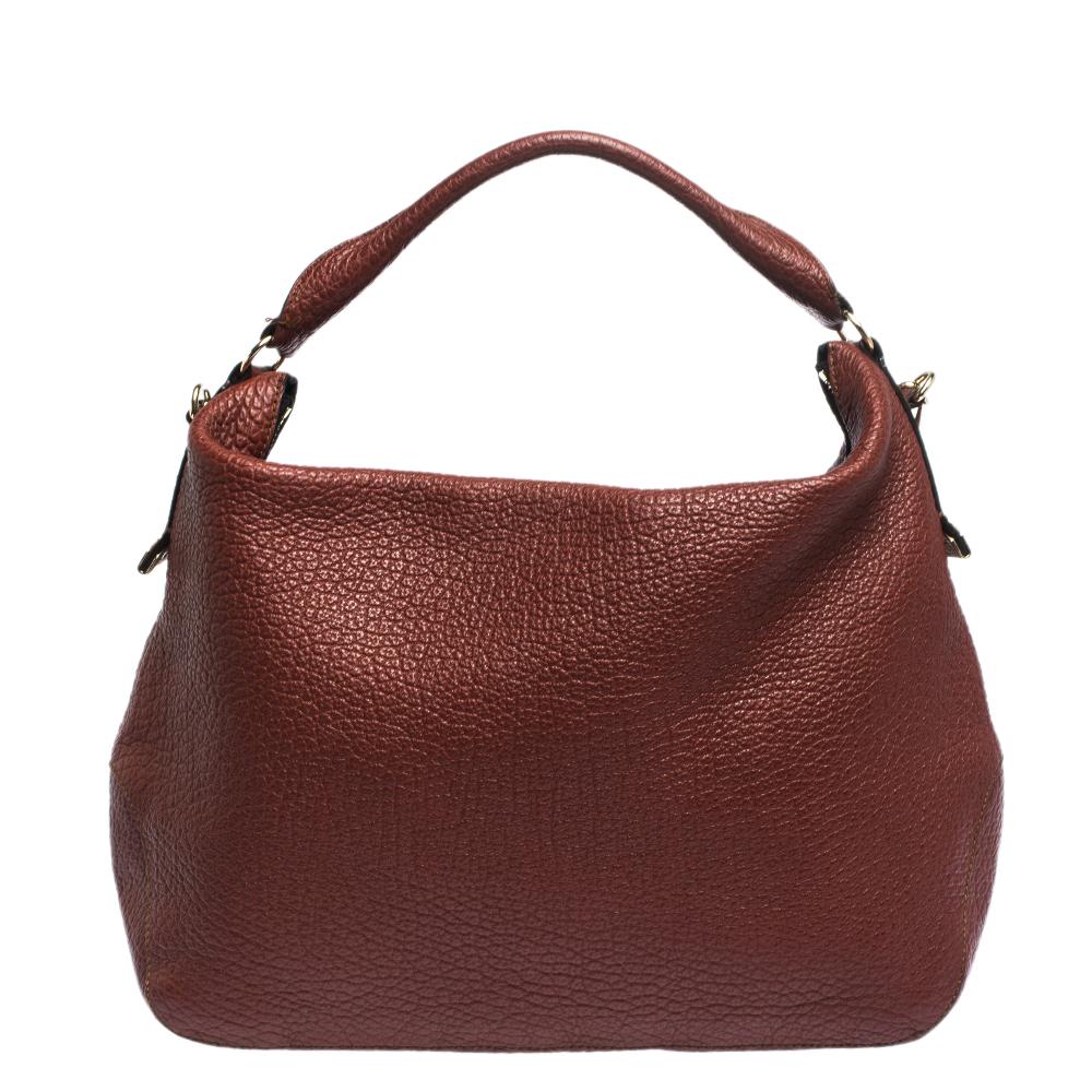 The British House of Burberry is known for excellence. This hobo is no different. Crafted from quality leather, it comes in a striking shade of brown. It is styled with a single handle, a shoulder strap and gold-tone hardware. The zip closure leads