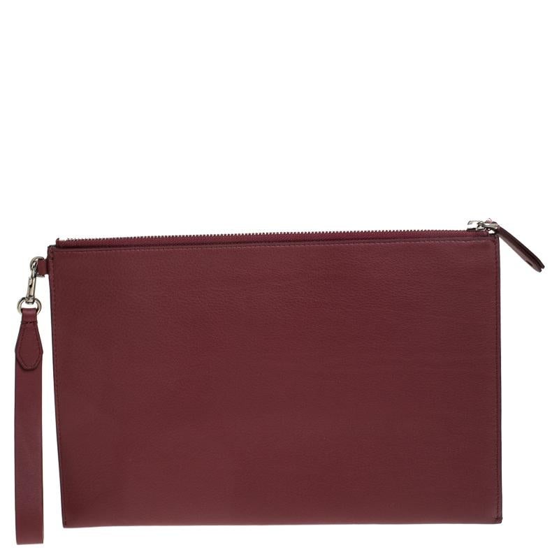 This stunning pouch by Burberry exudes class and sophistication. Crafted from leather, it comes in a stunning burgundy color. It features a top zip closure, leather interior sized to hold your essentials, a wristlet is attached to it with