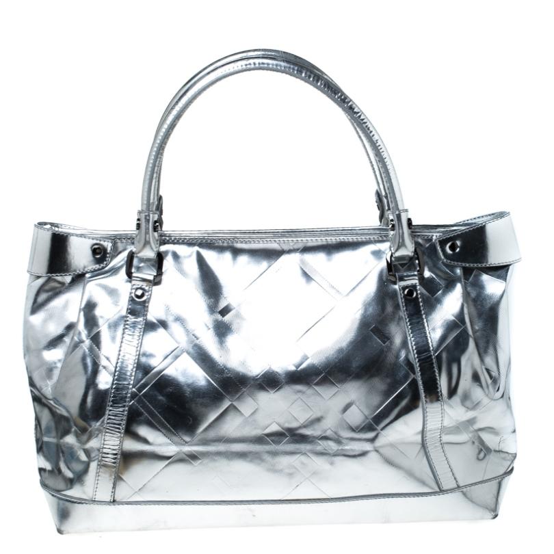 The perfect choice for special occasions, this Burberry tote is true to its existence. Crafted from metallic silver patent leather the bag is fabulously built and extremely alluring. Held by dual handles, it has a fabric lined interior secured by a