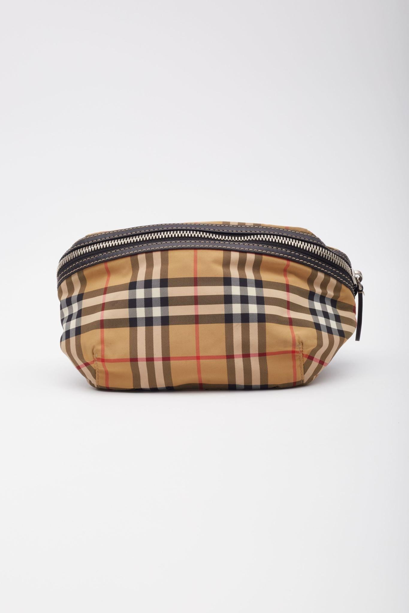 This belt bag is made of classic Burberry check in nylon with blue leather zipper pulls. This bag features a rear zipper pocket and adjustable canvas strap. The top zipper opens to a black fabric interior with a black leather patch pocket.

Color: