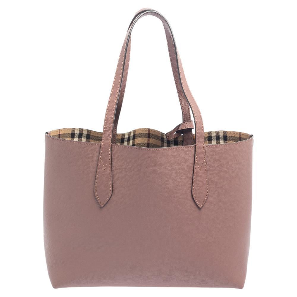 Catering to your changing moods, this Reversible tote from Burberry has been fabulously crafted in a reverse design so you can use it both ways. It comes with a pink leather body on one side and a checked coated canvas on the other. This tote is