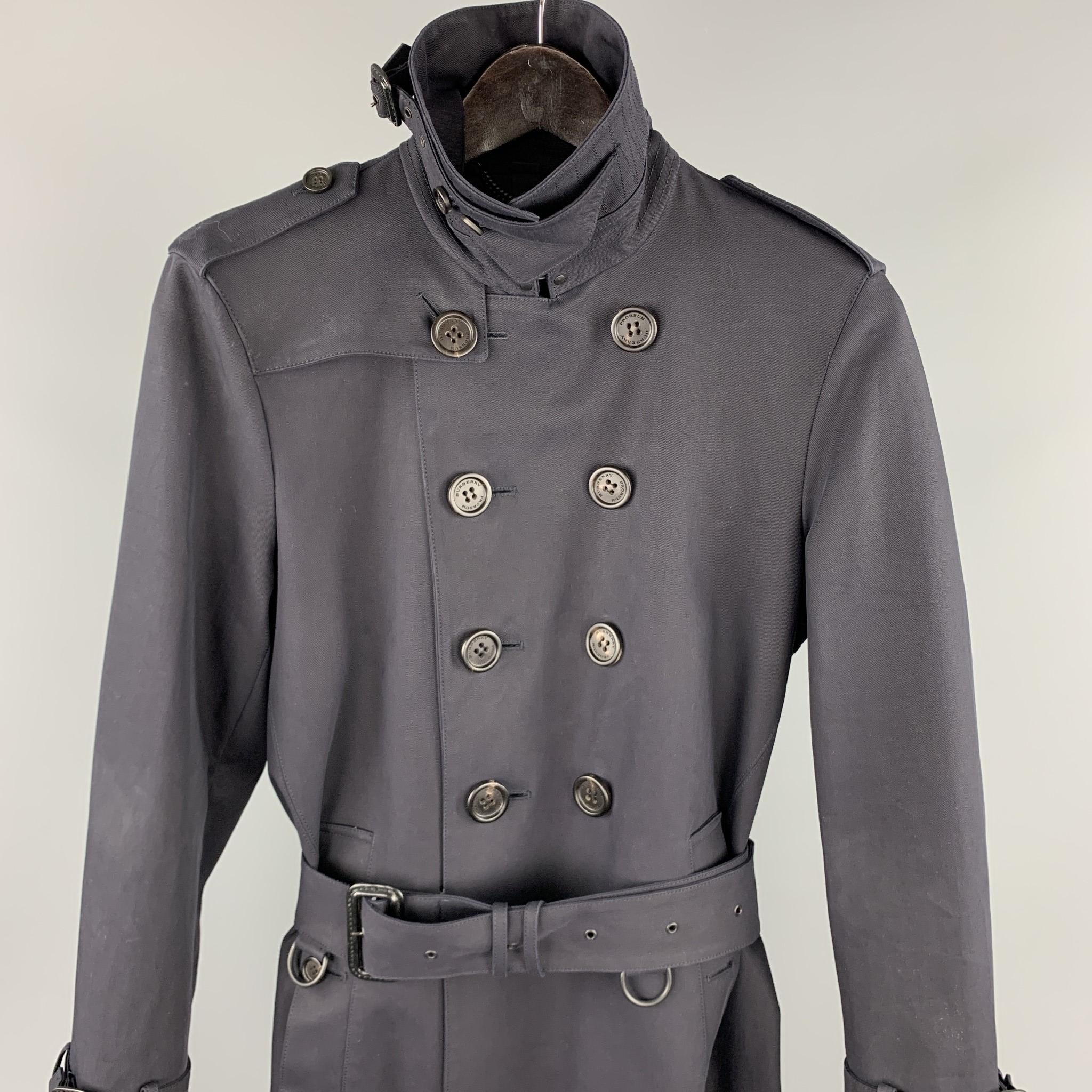 BURBERRY PRORSUM trench coat comes in a navy cotton with a full black monogram print liner featuring a belted style, high collar design, epaulettes, belted sleeve details, hook & eye, back vent, and a double breasted closure. Comes with dust bag.