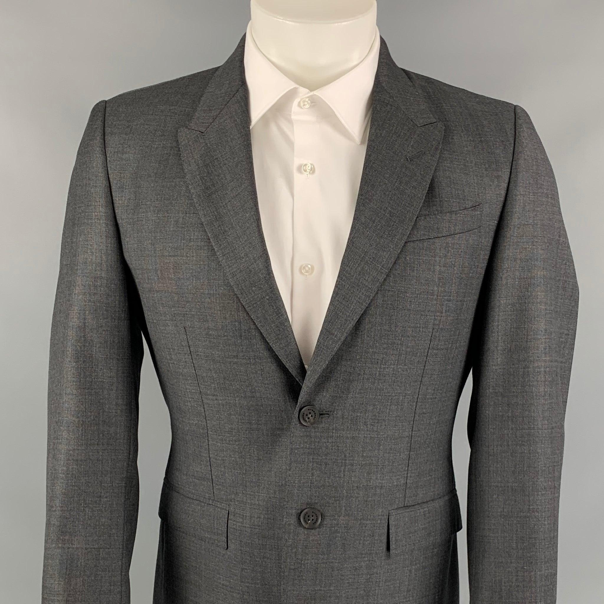 Le manteau de sport PRORSUM de Burberry se décline en gris ardoise avec un imprimé monogramme intégral. Il présente une coupe ajustée, un revers en pointe, des poches à rabat, une double fente au dos et une fermeture à deux boutons. Fabriquées en