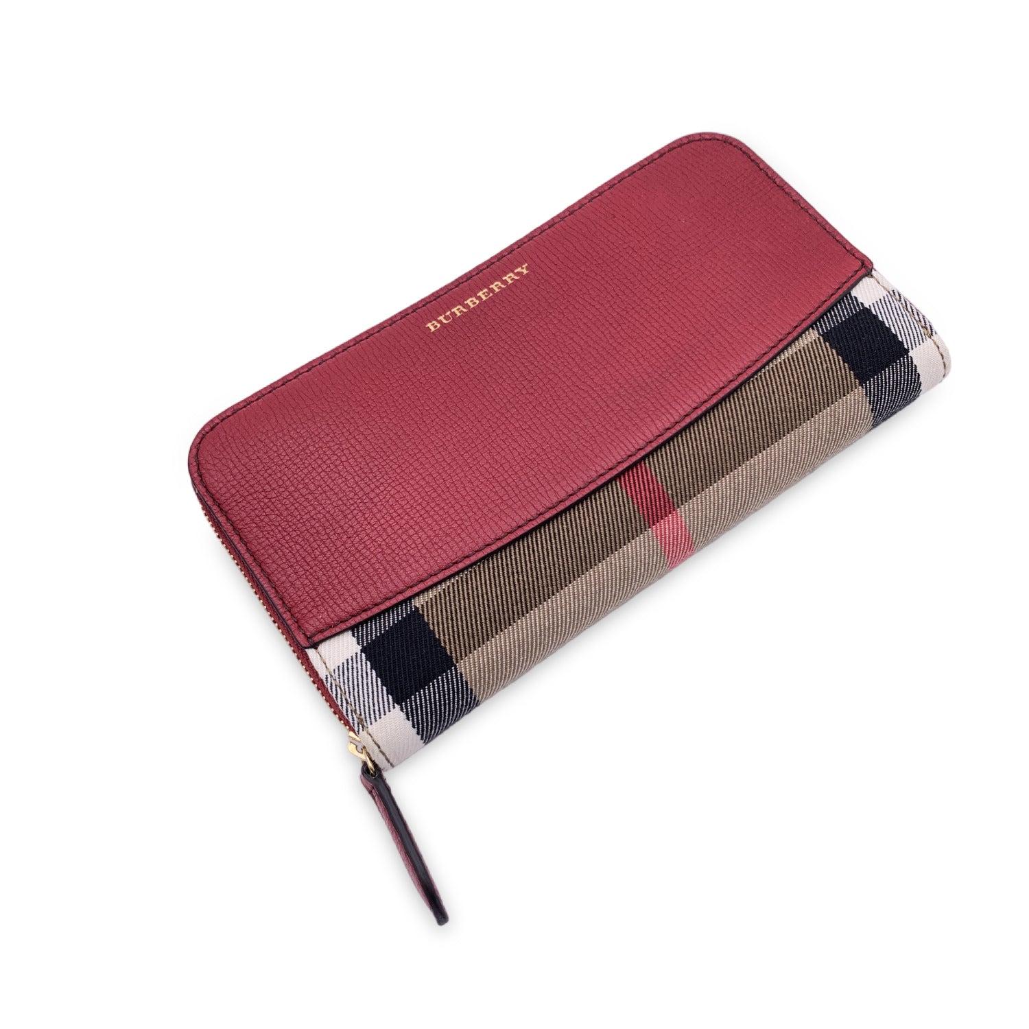 Burberry 'Elmore' Zippy Wallet crafted in checkered nova check canvas and red leather. Zip closure. Burberry signature embossed on the front. It features 2 main compartments for bill, 2 flat open pockets, 1 zip coin compartment, 12 credit card