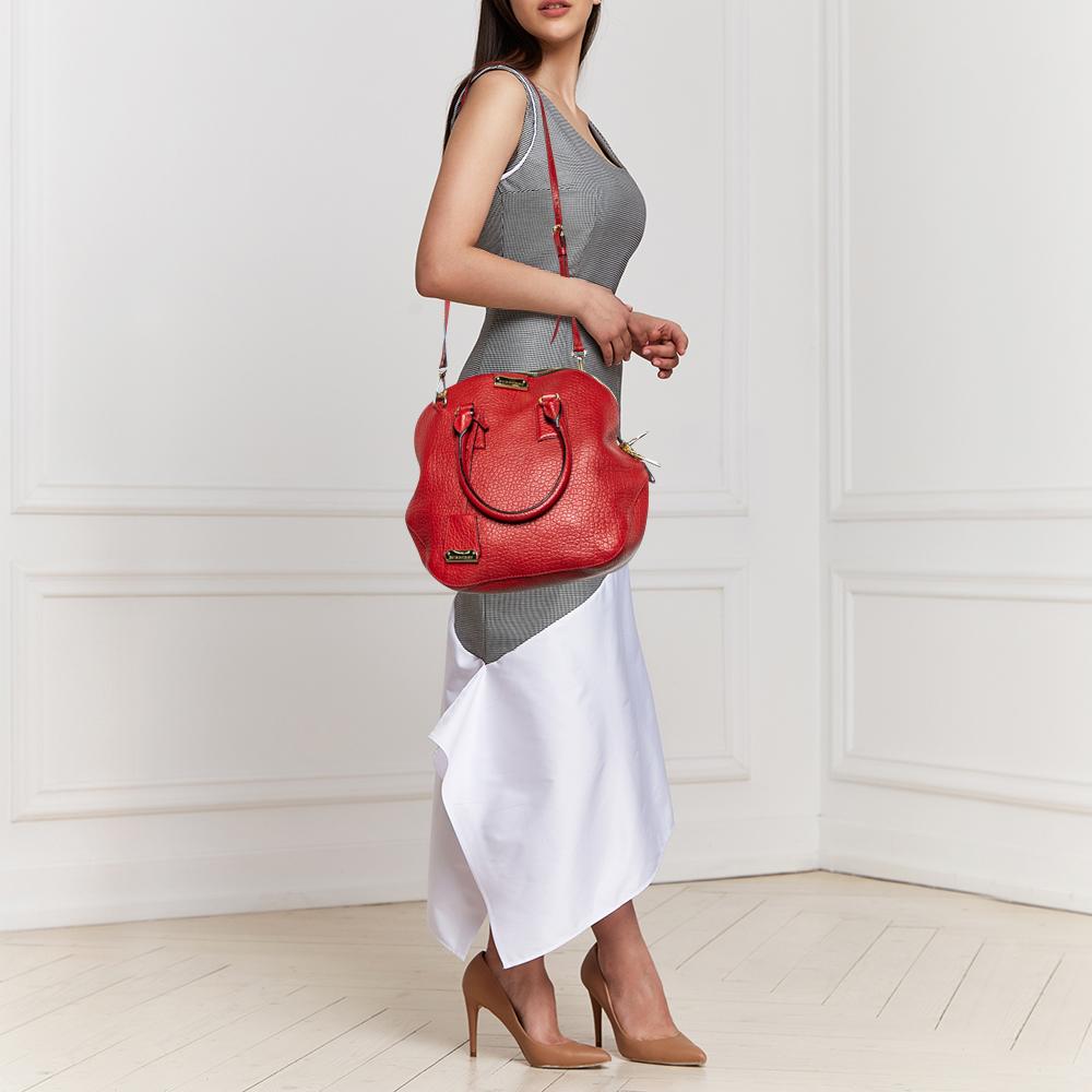 
This Burberry bag is distinguished by its unique silhouette. Made from red leather, it exhibits a single handle, a shoulder strap, and gold-tone hardware. The fabric-lined interior of the bag has more than enough space to accommodate your daily