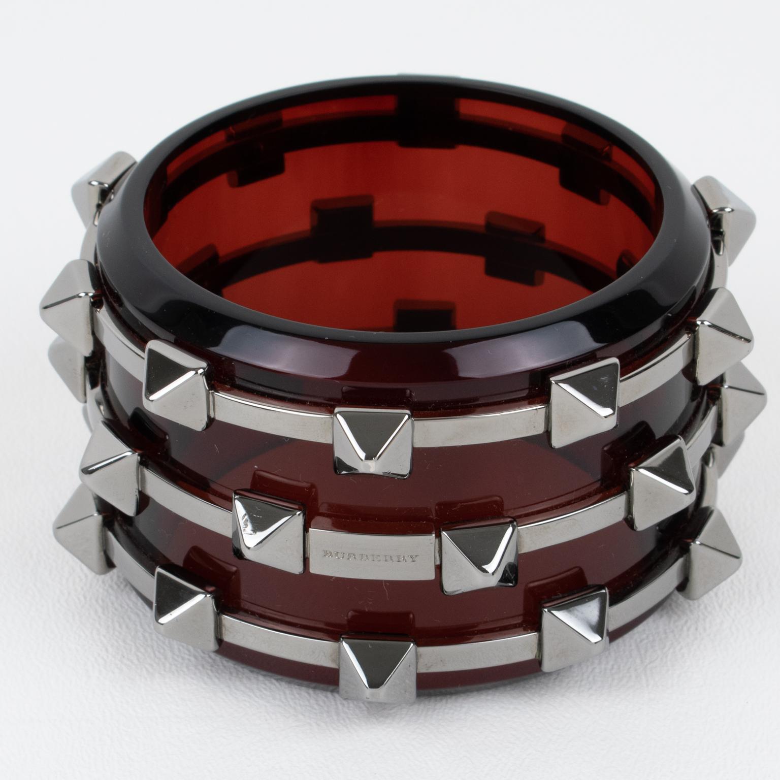 Magnifique bracelet en acrylique massif et métal de Burberry. Burberry revisite le design punk des manchettes dans une version chic et couture. Forme trapue avec des bracelets en Perspex ou en acrylique rouge bordeaux avec des anneaux et des pointes