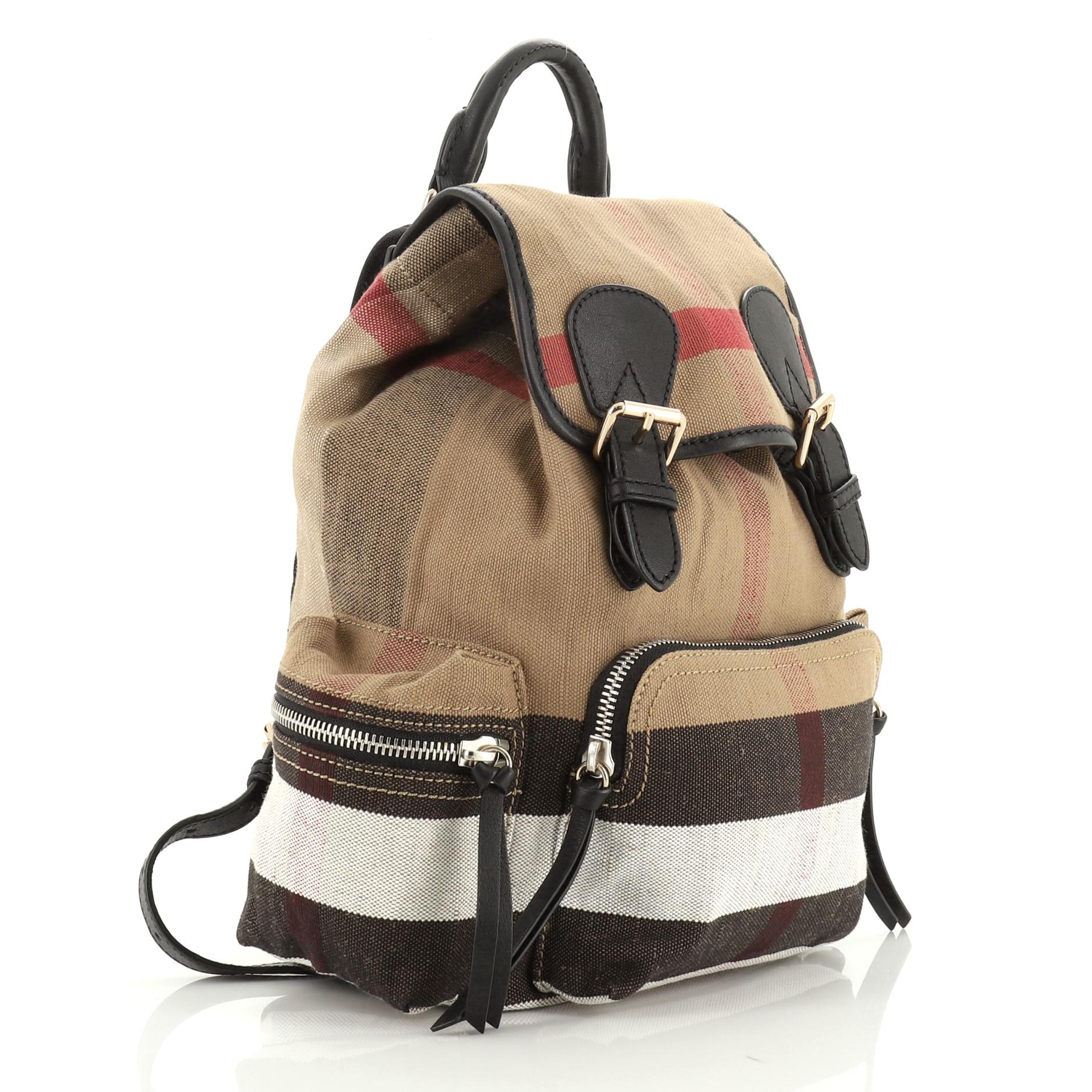 This Burberry Rucksack Backpack House Check Canvas Medium, crafted from multicolor house check canvas, features a leather top handle, adjustable shoulder straps, exterior zip pockets, quilted back panel, and gold and silver-tone hardware. Its