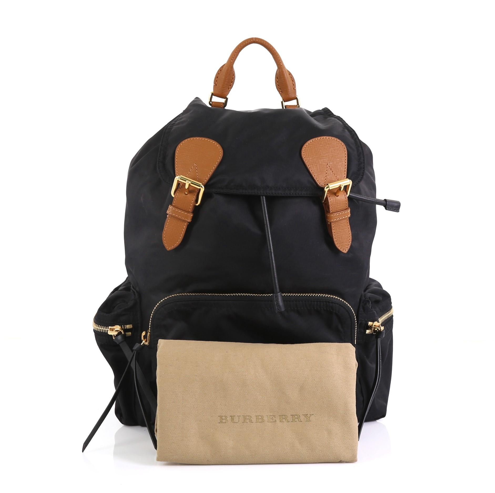 This Burberry Rucksack Backpack Nylon with Leather Large, crafted from black nylon, features a leather top handle, adjustable shoulder straps, exterior zip pockets, quilted back panel, and gold-tone hardware. Its drawstring under snap-tab flap