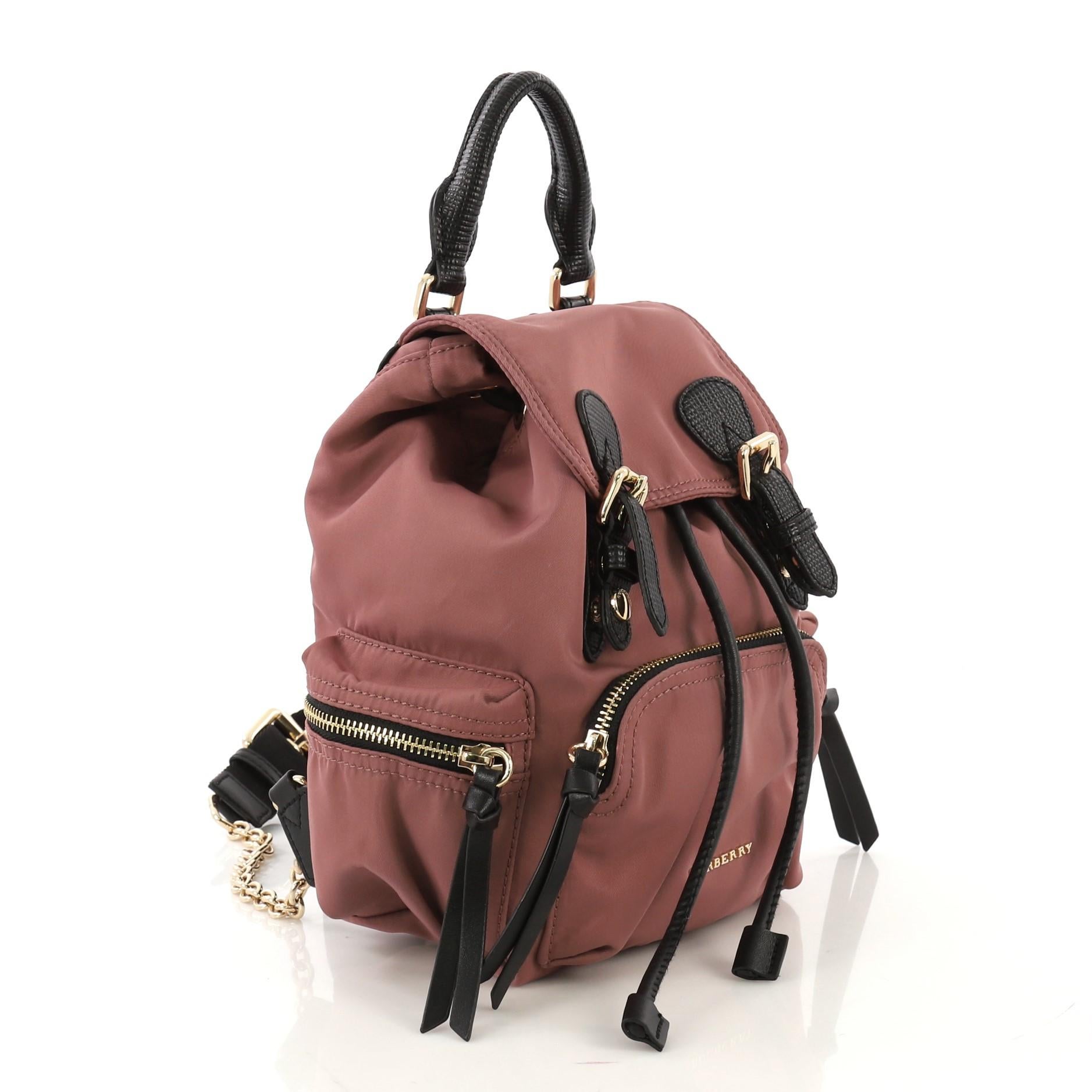 This Burberry Rucksack Backpack Nylon with Leather Small, crafted from dusty pink nylon with black leather, features a leather top handle, adjustable shoulder straps, exterior zip pockets, quilted back panel, and gold-tone hardware. Its drawstring