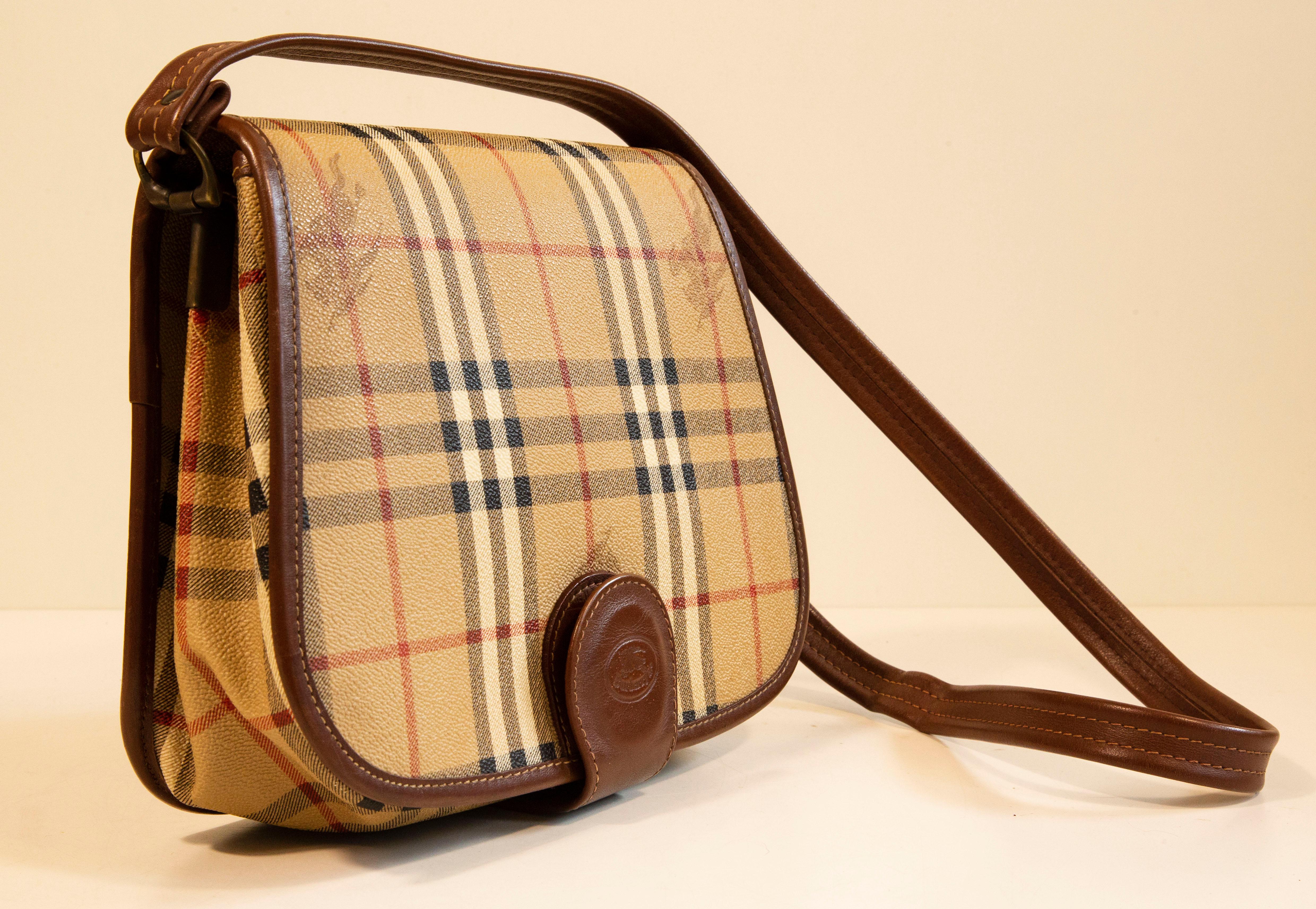 A vintage Burberry saddle bag made of coated canvas with the Burberry classic check print and brown leather trim. The brown leather shoudlers strap is adjustable in length, max 105 cm. The interior is divided  into two compartments by a zipped