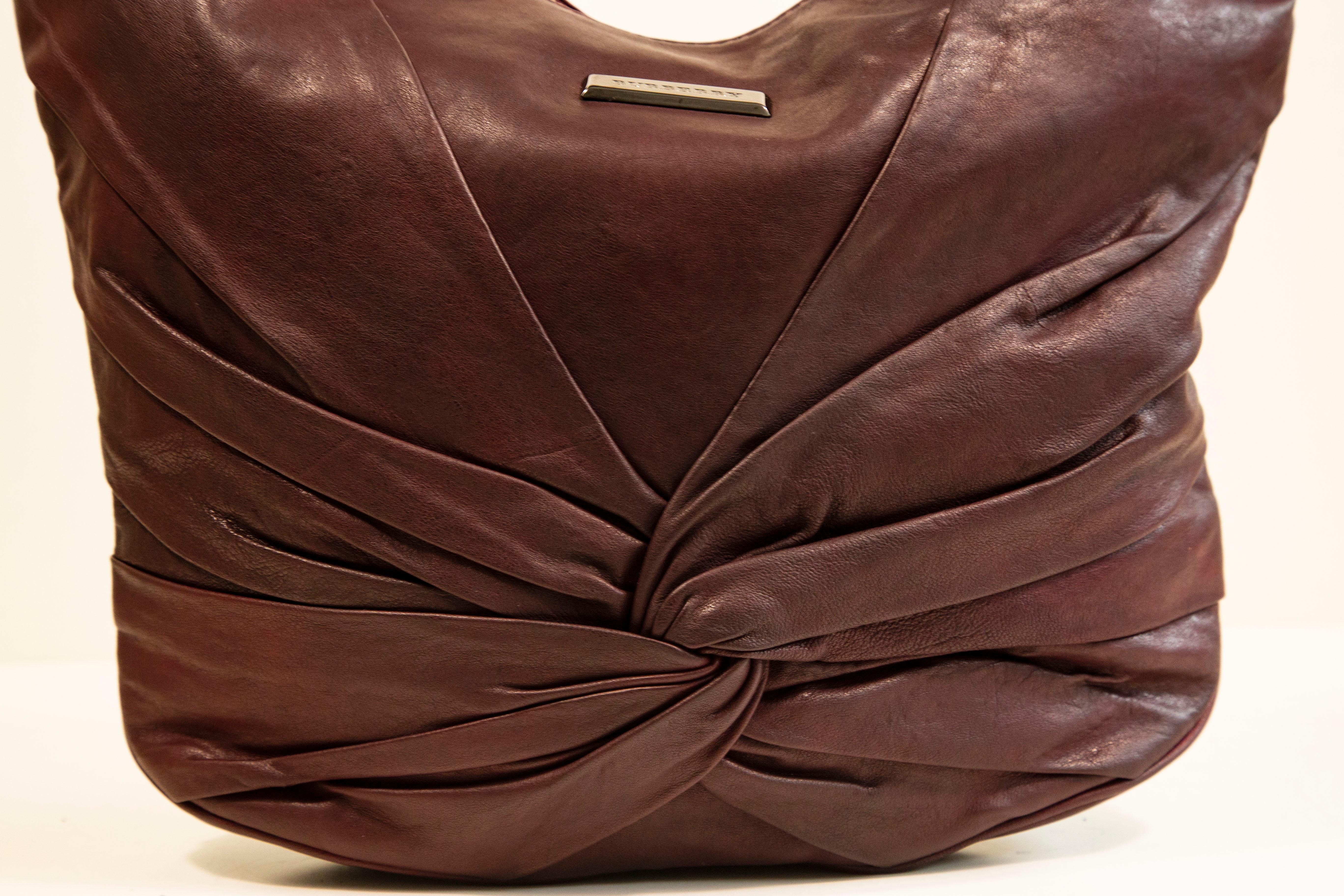 Burberry shoulder bag made of burgundy leather with pewter toned hardware. The interior is lined with the Burberry check canvas, and next to the major compartment it features three side pockets of which one has a zipper. The bag has hardly any signs