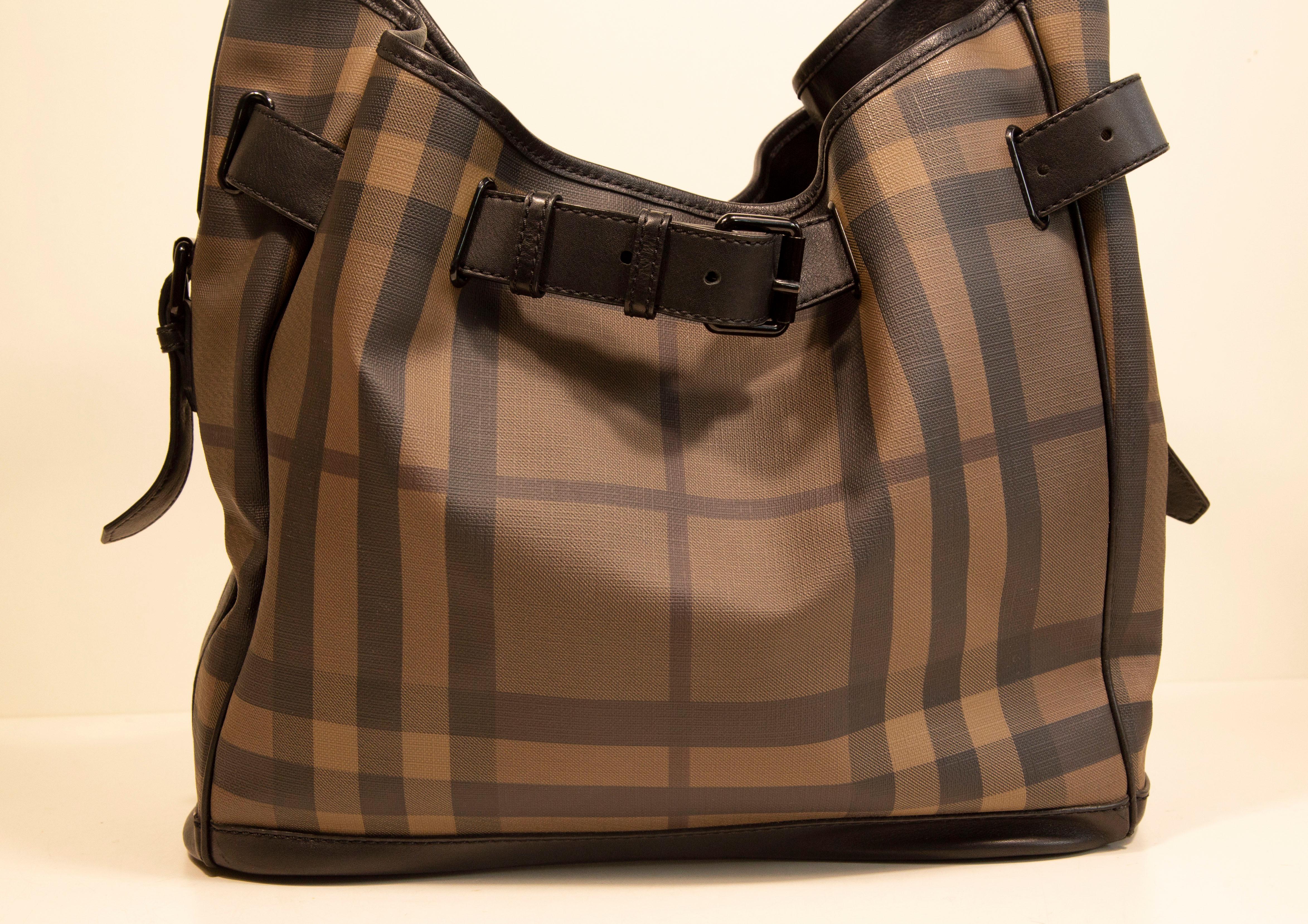 An authentic Burberry shoulder bag. The bag features a black/gray  check canvas exterior, black leather trim, and black-toned hardware. The interior is lined with black fabric and is separated into two main compartments by a zipped pocket