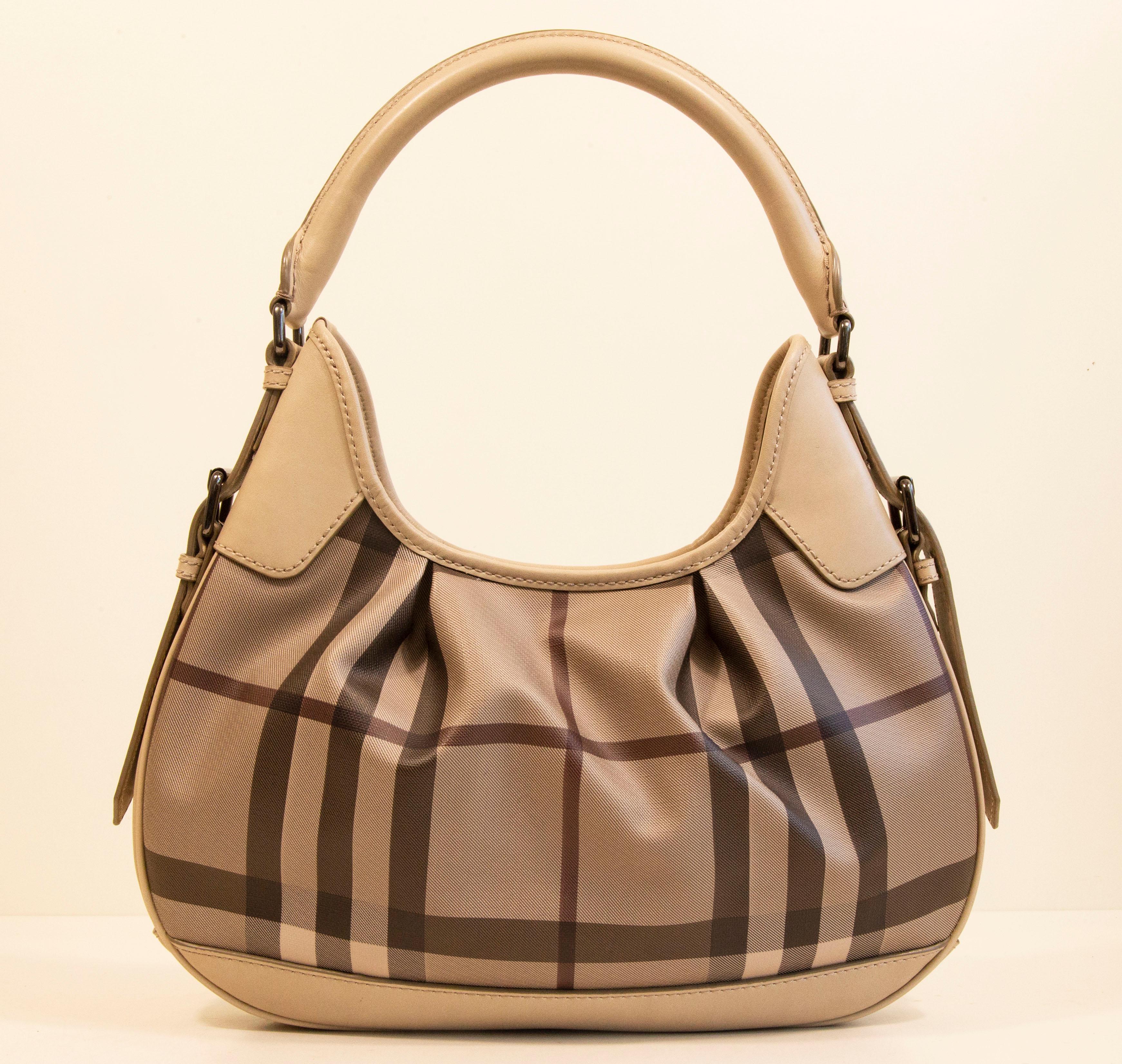A Burberry shoulder bag made of coated multicolor canvas with light gray leather trim, and shiny pewter toned hardware. The exterior features the Burberry Nova Check pattern,  The interior is lined with brown fabric and next to the major compartment