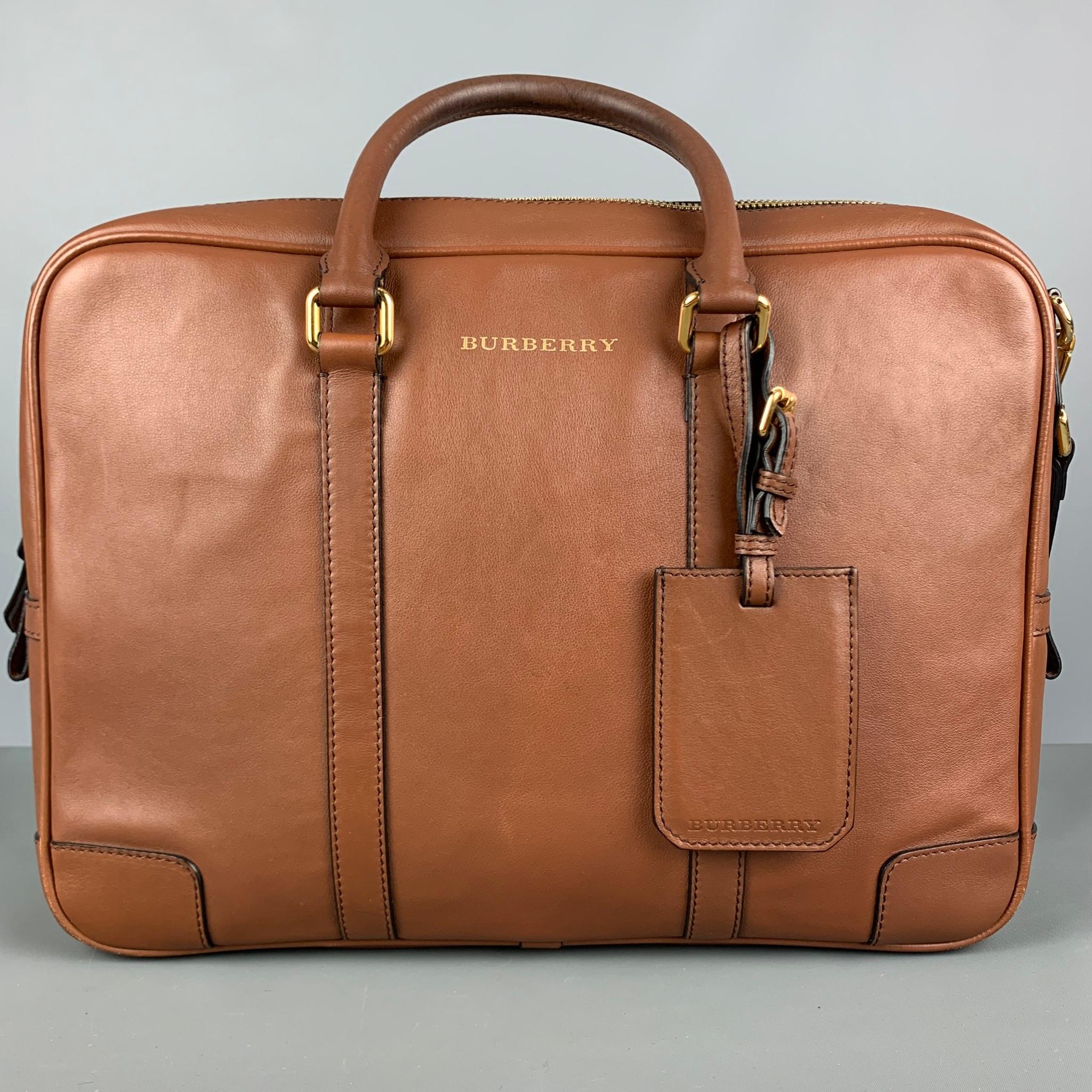 BURBERRY briefcase come in tan leather material featuring a detachable shoulder strap, gold tone hardware, inner pocket and inner slots, luggage name tag, Burberry signature plaid lining, and a zipper closure. This item comes with dust bag. Made in