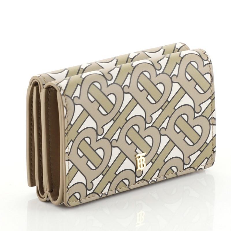This Burberry TB Double Flap Wallet Monogram Print Leather, crafted from neutral printed leather, features gold-tone hardware. Its flap with snap button closure on both sides opens to a brown leather interior multiple card slots and slip pockets.