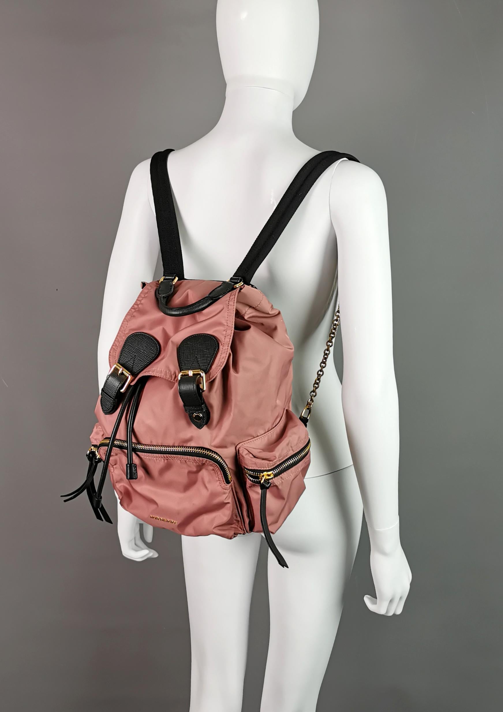 You gotta love this stylish and luxe rucksack or backpack by Burberry!

This backpack is from the Burberry The Rucksack range and is finished in a lovely dusky pink nylon with black accents and gold tone metal hardware, the colours work so well