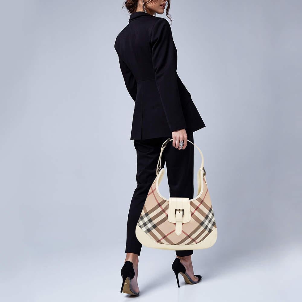 This Brooke hobo bag from the luxury fashion house exudes unmatched elegance. It is crafted from Burberryâ€™s signature check PVC and patent leather. It has a buckle flap closure and flat shoulder handle with a buckled detail. Its fabric lined