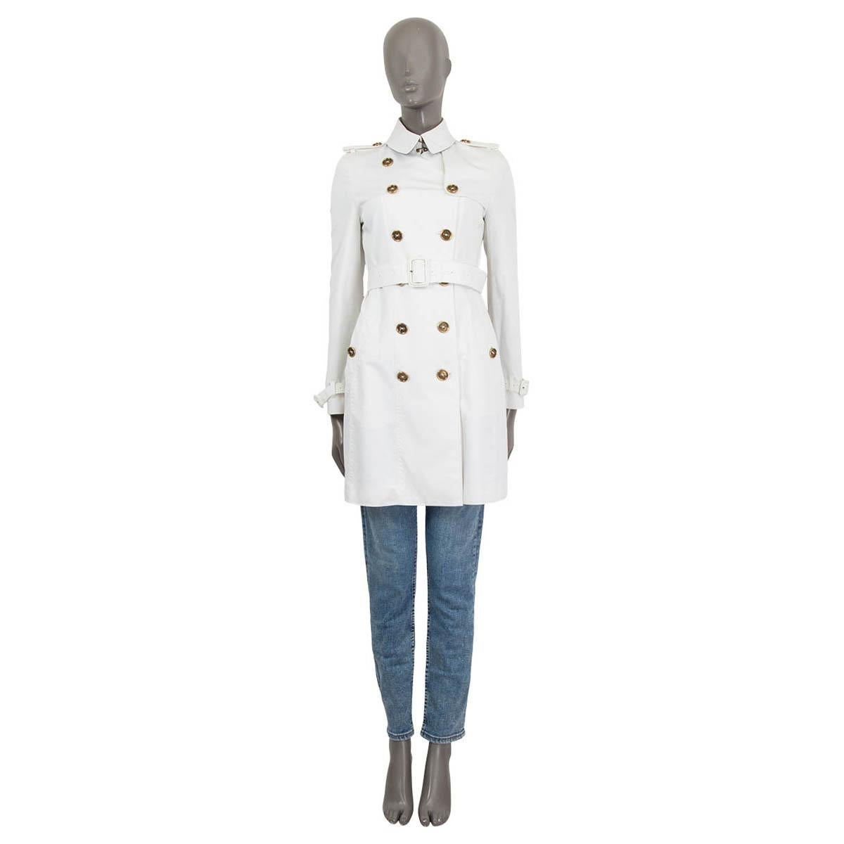 100% authentic Burberry London double-breasted short trench coat in white cotton (98%) and elastane (2%) with belted cuffs and shoulder epaulettes. Closes with one hook at the neck, six buttons on the front and a detachable belt at the waist-line.