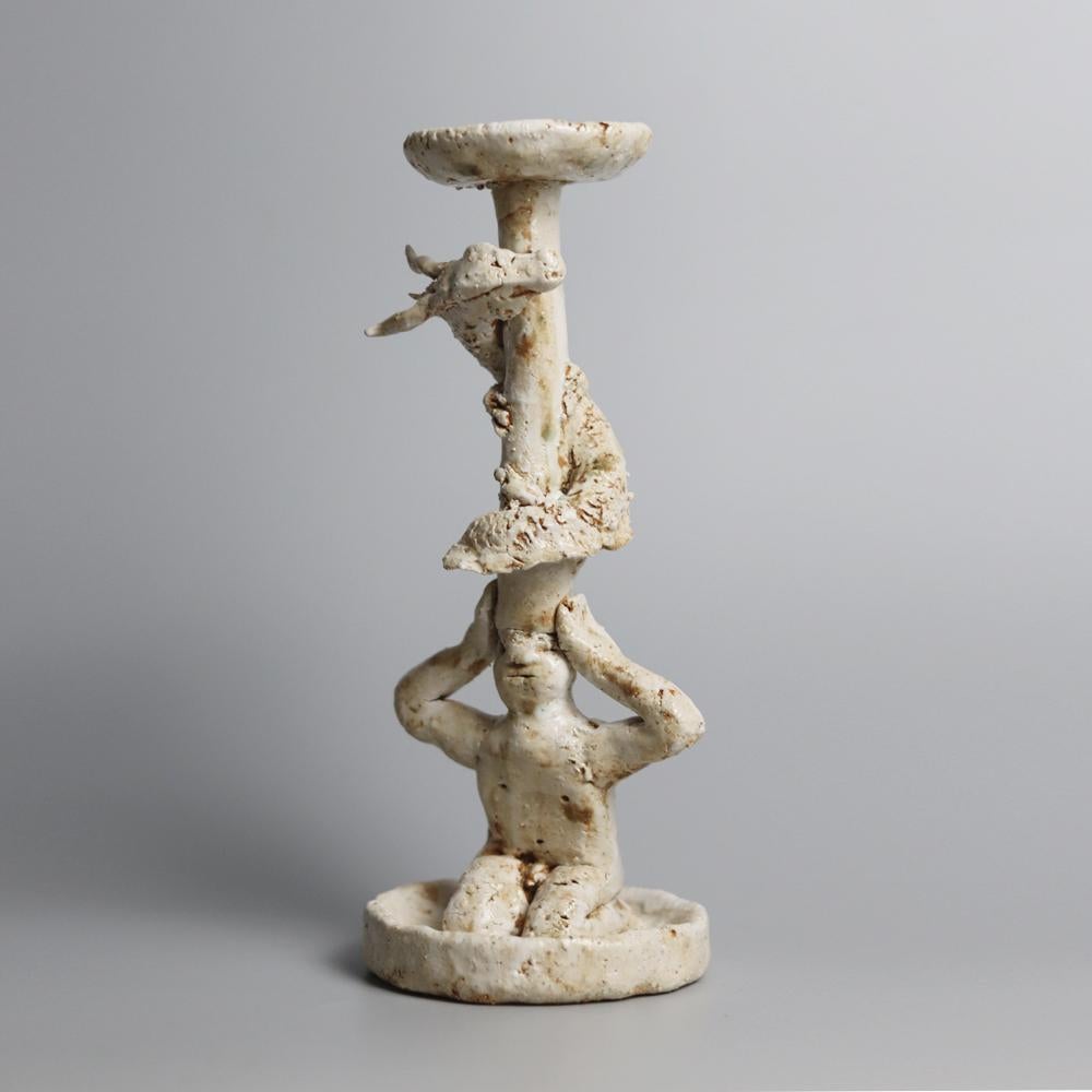 Burden and Flame is a sculptural ceramic candle holder by Chinese artist Darren Dai. The work intertwines mythology, ritual, and the quiet weight of devotion. A seated figure supports a rising pillar on its head, a form that becomes both burden and
