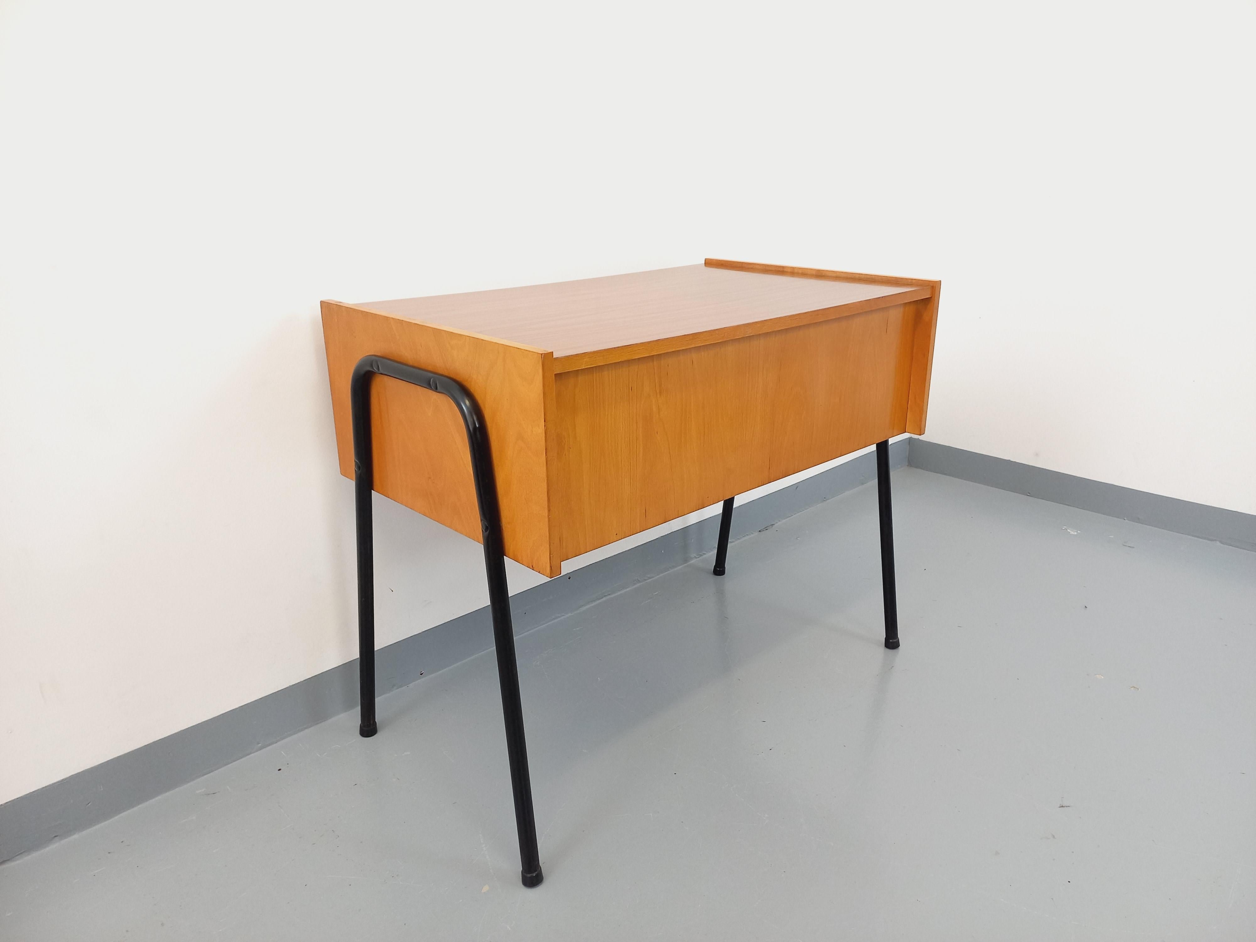 Bureau vintage des années 60, style moderniste dans le goût de Pierre By, plateau en mélaminé imitation bois, piétement métallique noir design, structure en bois clair avec niche et 2 tiroirs à boutons en métal. Bon état général avec quelques signes