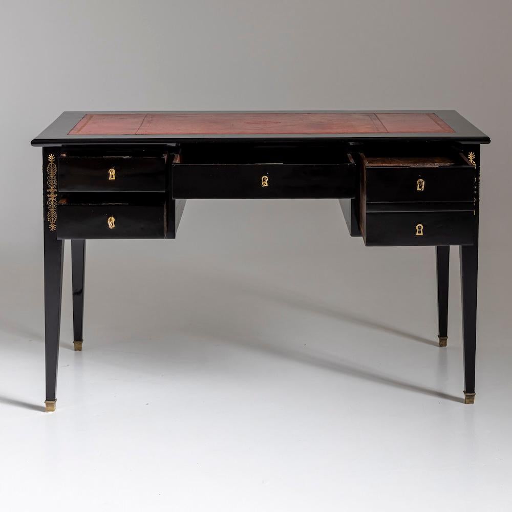 Piccolo bureau plat ebanizzato della fine del XIX secolo con superfici di scrittura rivestite in pelle rossa ed elementi decorativi dorati agli angoli. Il piano del tavolo è dotato di superfici di scrittura che possono essere estratte lateralmente.
