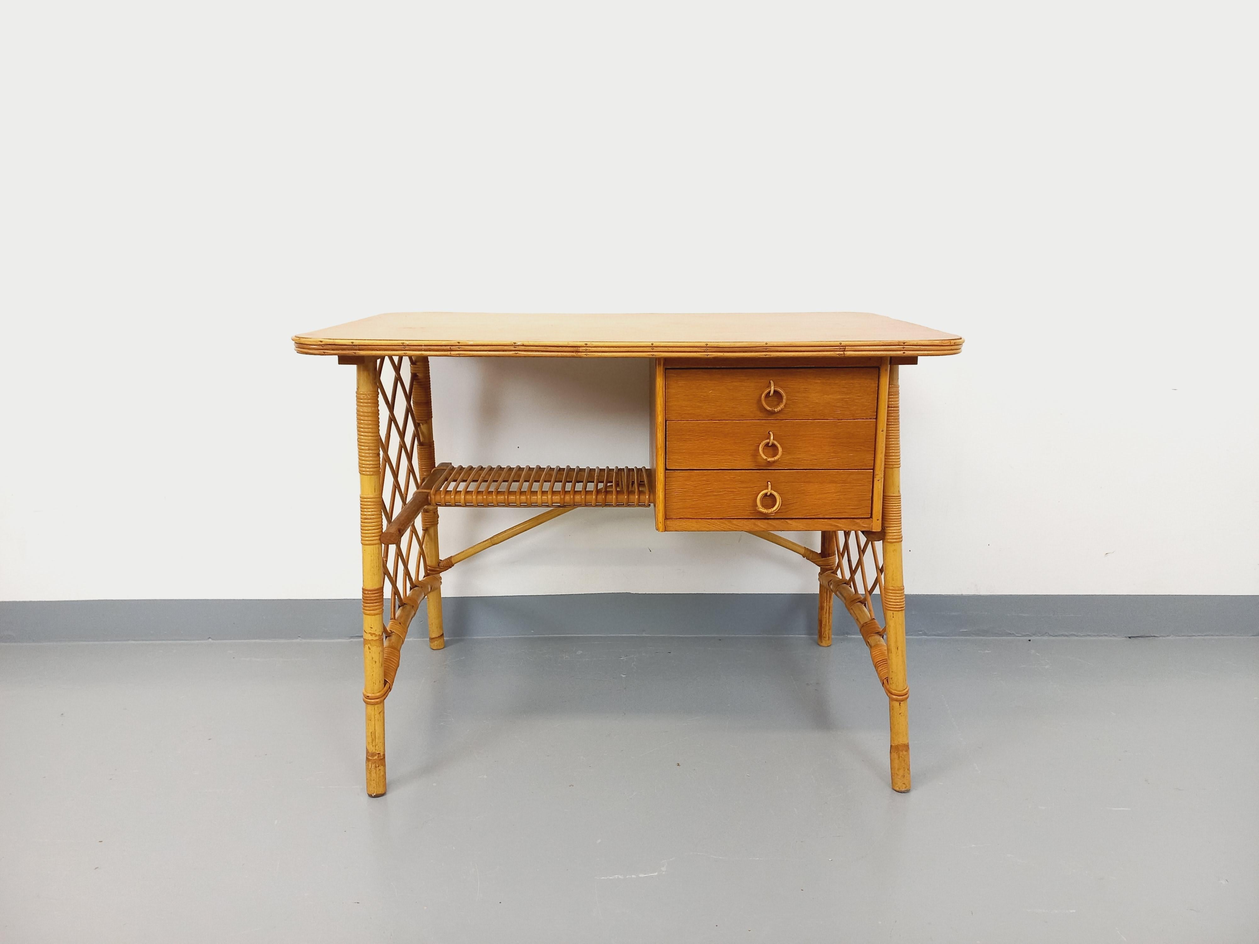 Bureau vintage des années 60, très joli design attribué à Louis Sognot, en rotin, plateau et tiroirs en bois de chêne, 3 tiroirs, très beau travail du rotin, très bon état général, plateau poncé et verni avec une marque restante. Es kann in der